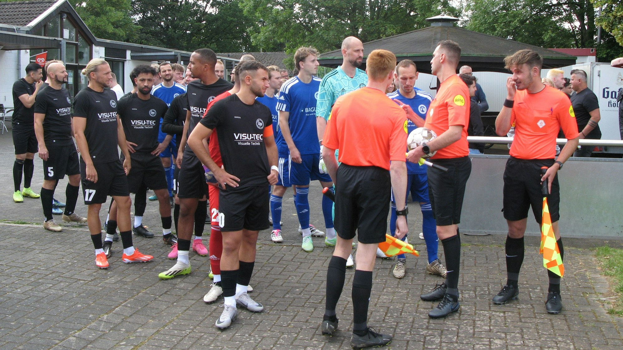 Die Fußballer aus Düsseldorf und Essen in schwarzen und blauen Trikots mit dem Schiedsrichtergespann vor dem Einlauf ins Hennefer Stadion.