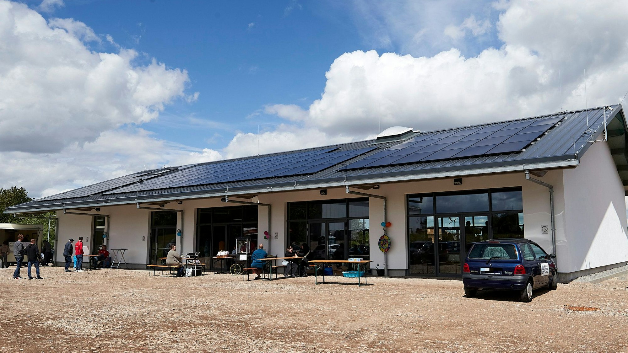 Der Neubau des Dorfgemeinschaftshauses Glehn hat PV-Anlagen auf dem Dach. Davor stehen Bierbänke für die Einweihungsfeier.