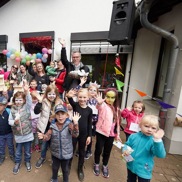 Kinder und Erwachsene stehen vor dem Kita-Gebäude, das mit Ballons und Wimpeln geschmückt ist.