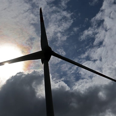 Eine Windkraftanlage ist vor einem leicht bewölktem Himmel im Gegenlicht zu sehen.