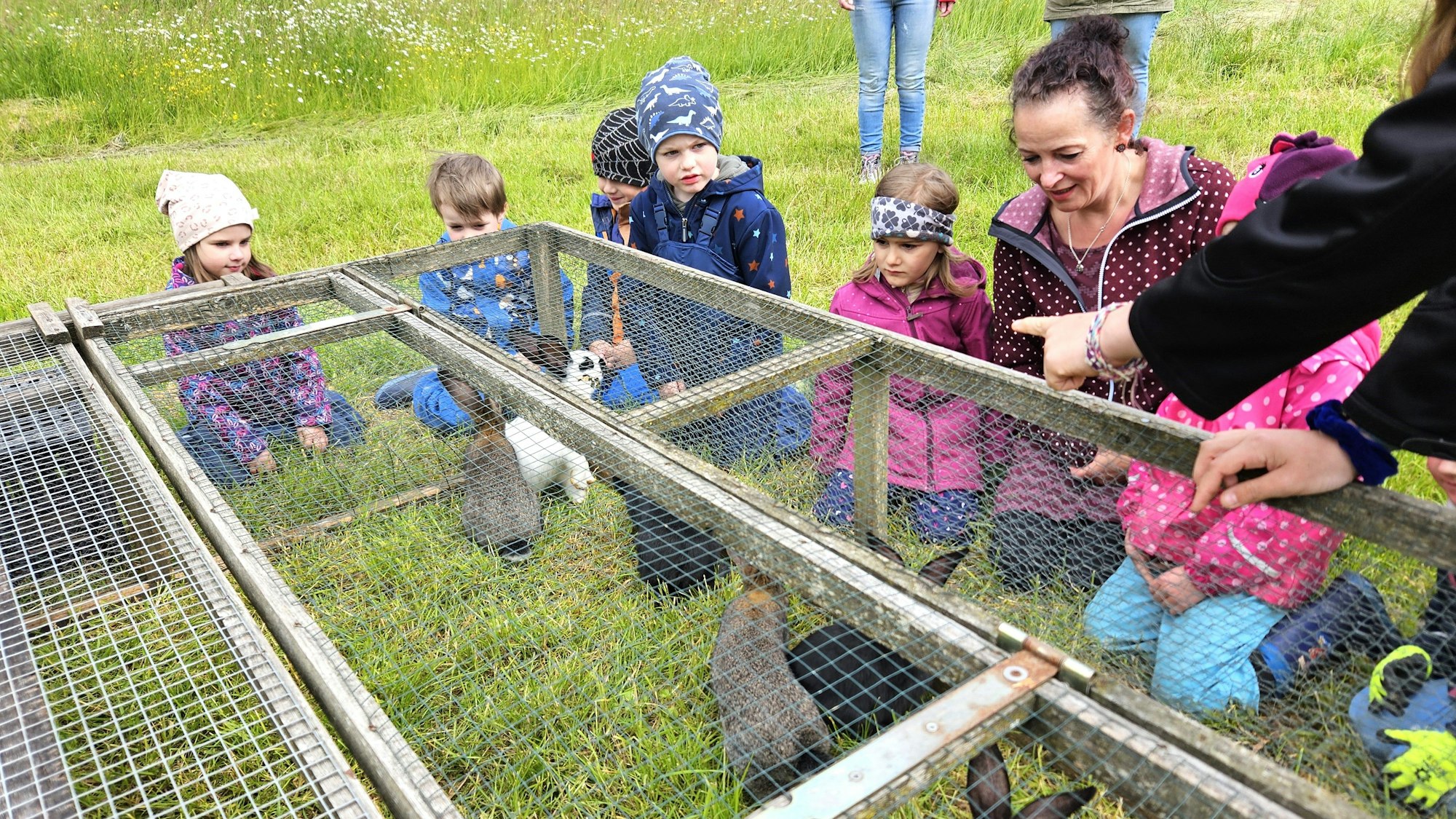 Die Kinder und eine der Erzieherinnen knien vor einem Stall mit Kaninchen.