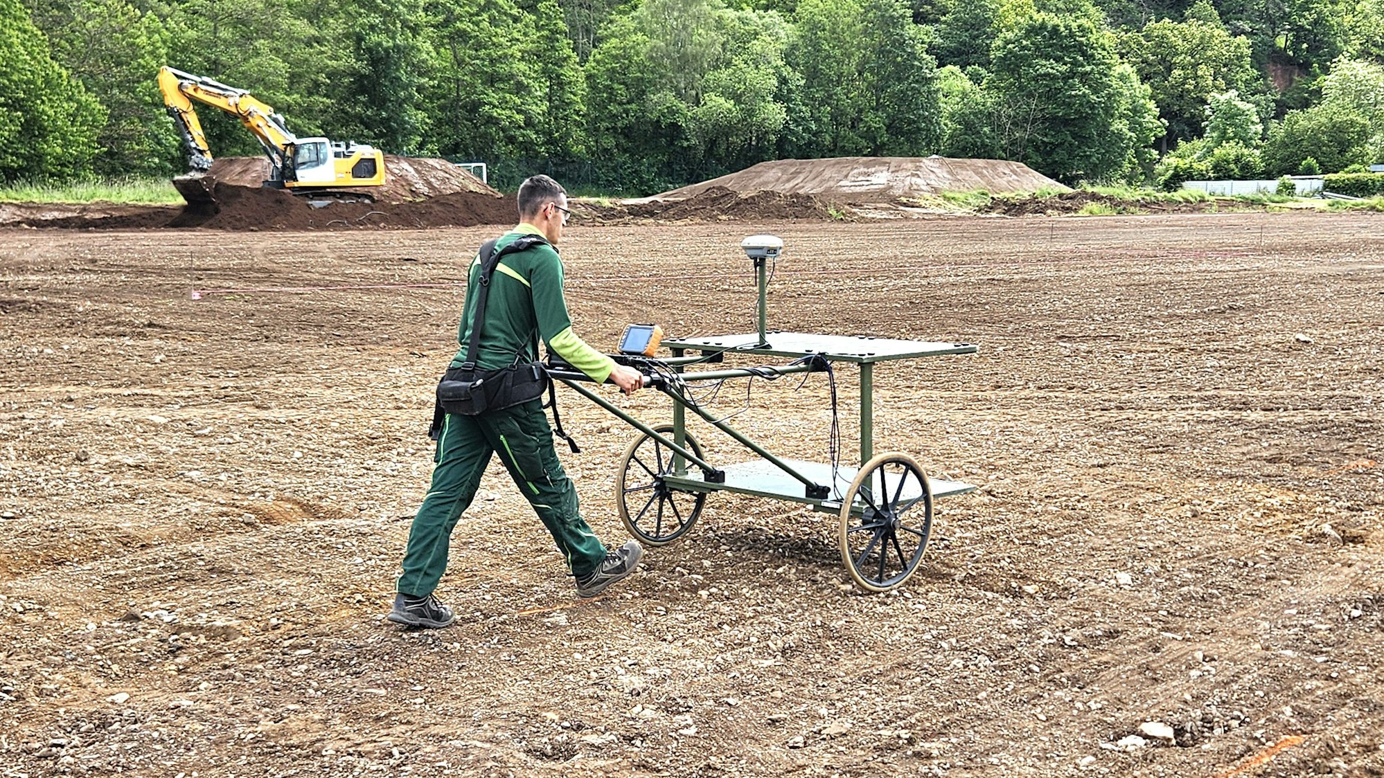 Ein Kampfmittelsondierer schiebt einen Wagen mit zwei Rädern über den ehemaligen Sportplatz.