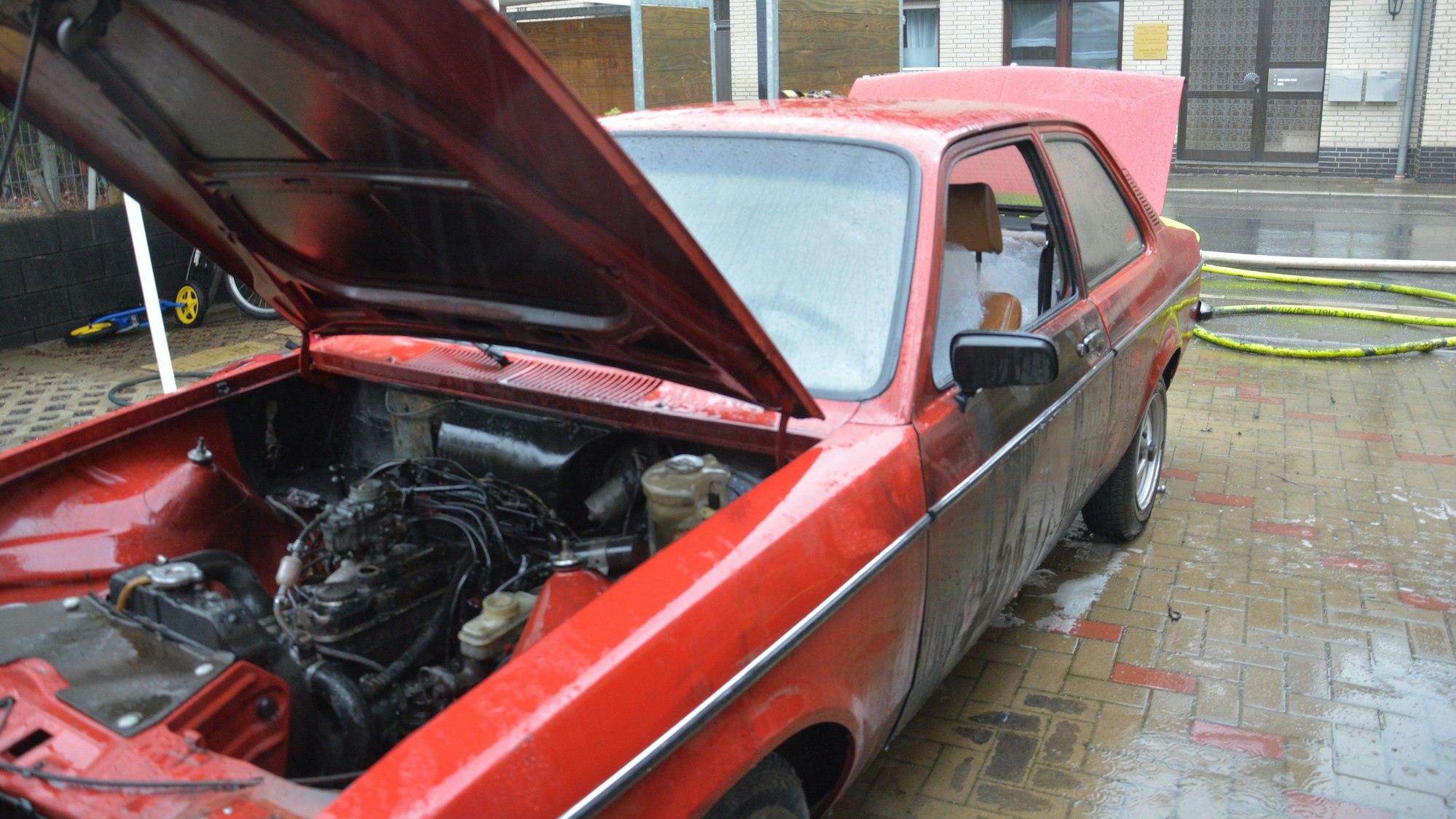 Ein roter Kadett steht mit offener Motorhaube auf einem Parkplatz.