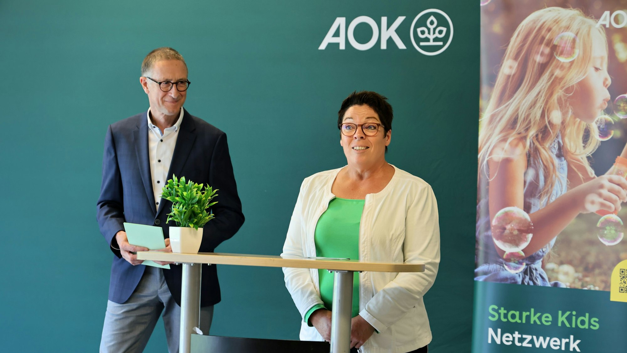 Die beiden Genannten bei der Begrüßung, im Hintergrund ein Themenplakat des „Starke Kids Netzwerks“.