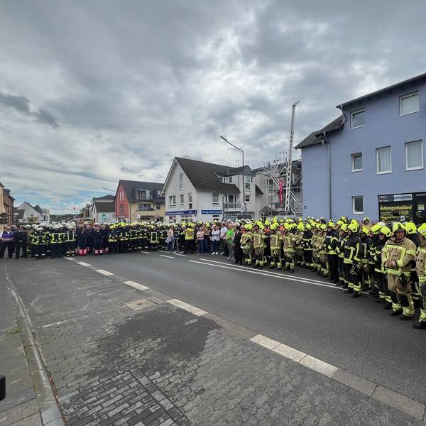 Viele Menschen, darunter hunderte Feuerwehrleute stehen auf einer Straße.