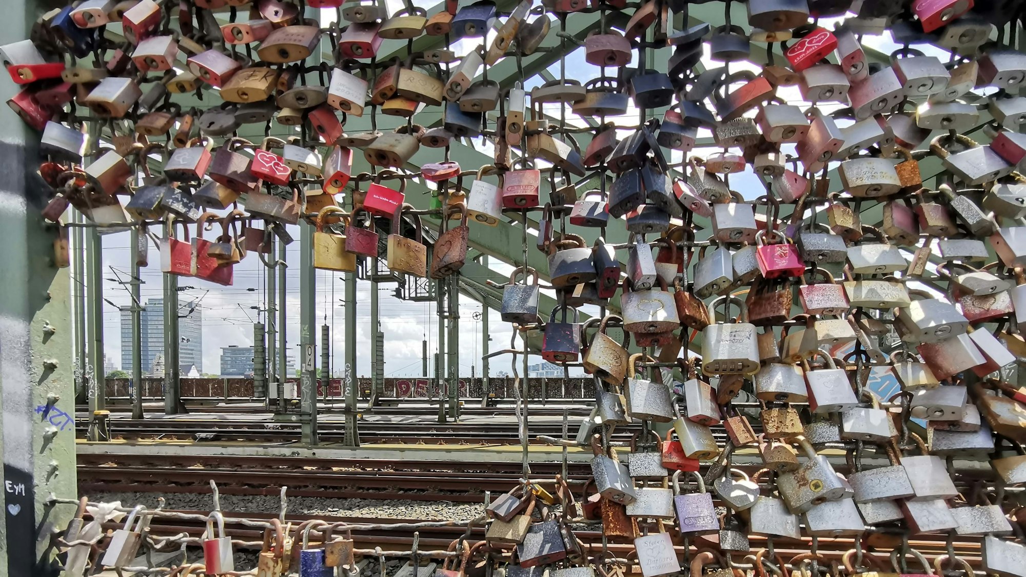 An der Kölner Hohenzollernbrücke hängen Liebesschlösser an einem beschädigten Drahtzaun.