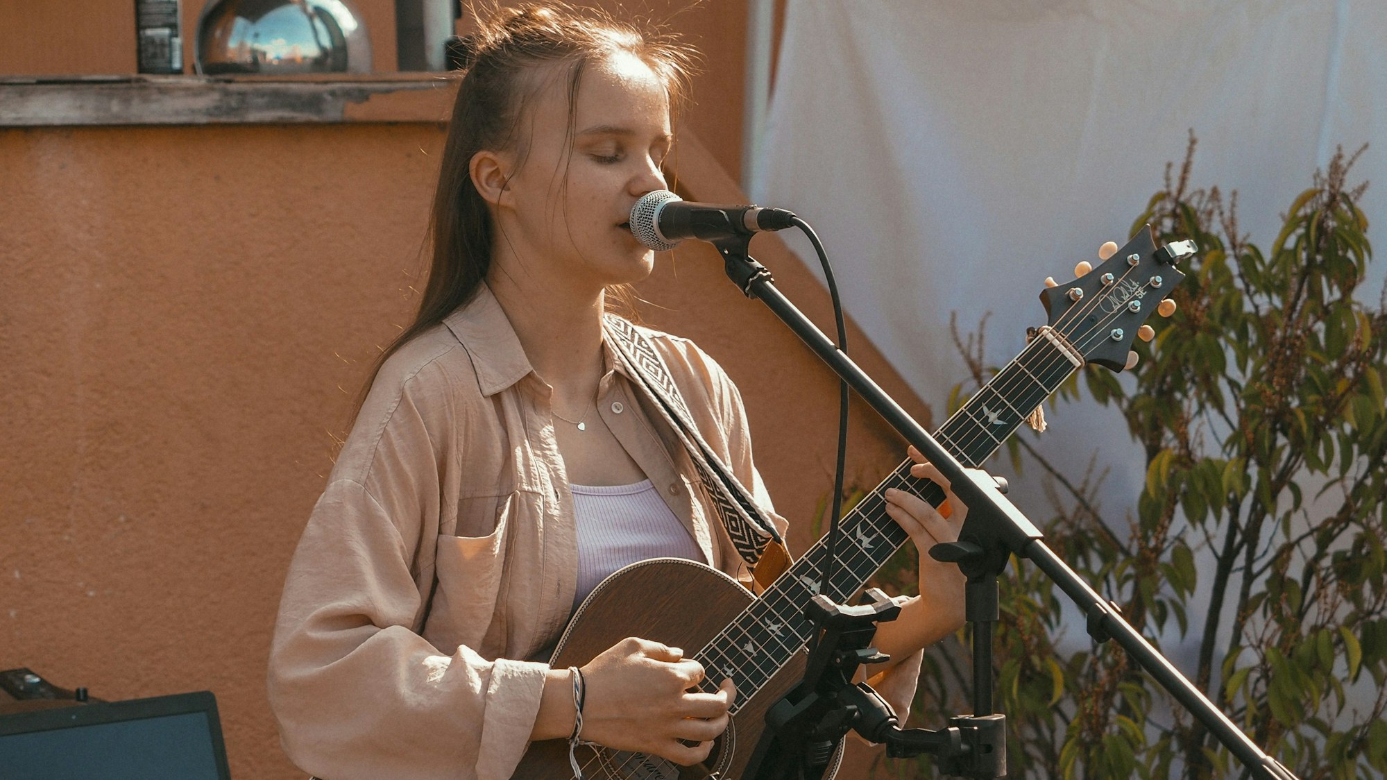 Kira Grohs steht mit einer Gitarre in der Hand vor einem Mikrofon und singt.