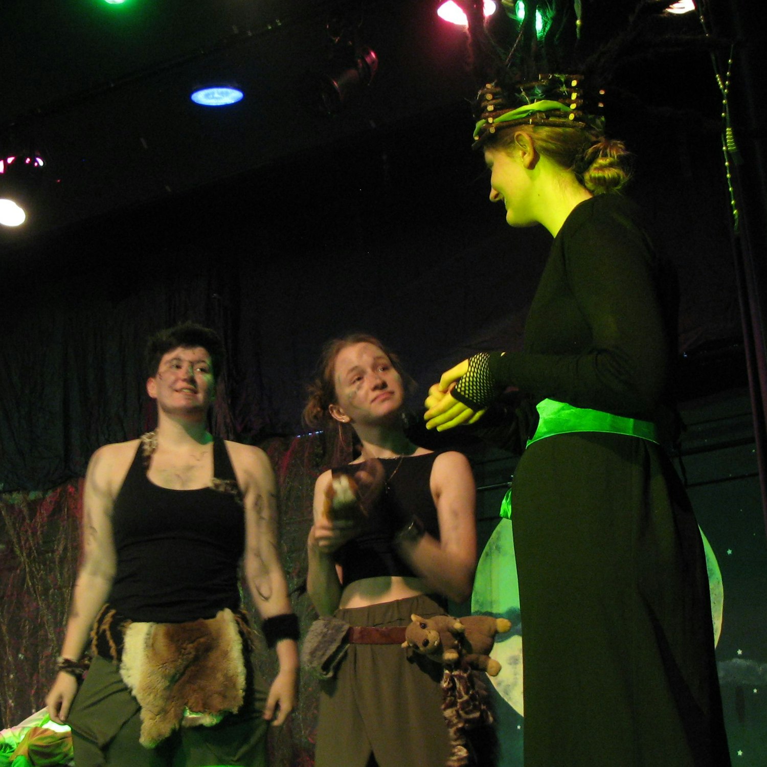 Die Darstellerin der Elfenkönigin Obera im schwarzen Gewand mit zwei Puck-Darstellerinnen.