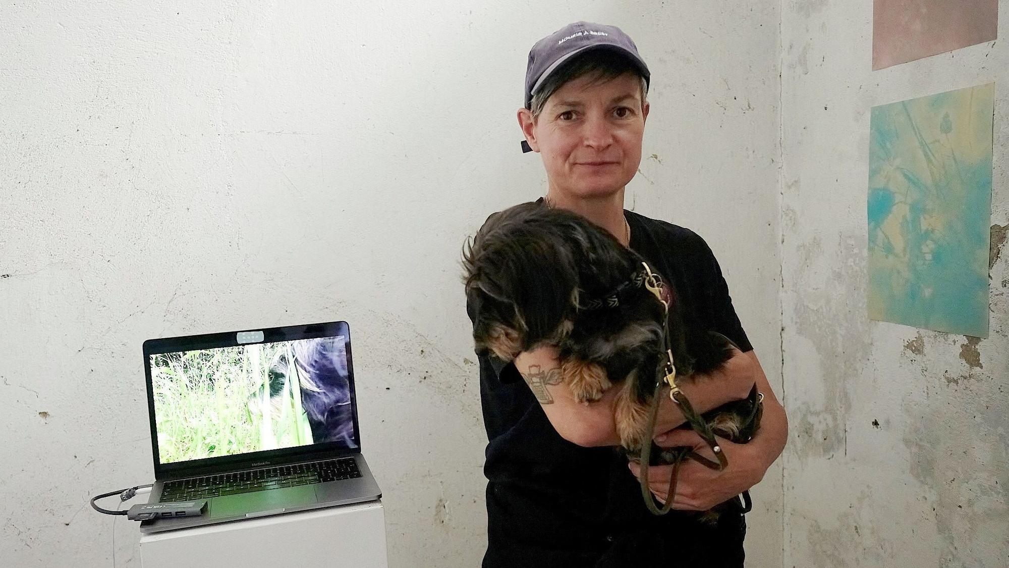 Jennifer De Negli hält einen Dackel auf dem Arm. Der hund schaut zu einem Laptop, der auf einem kleinen Tisch steht.