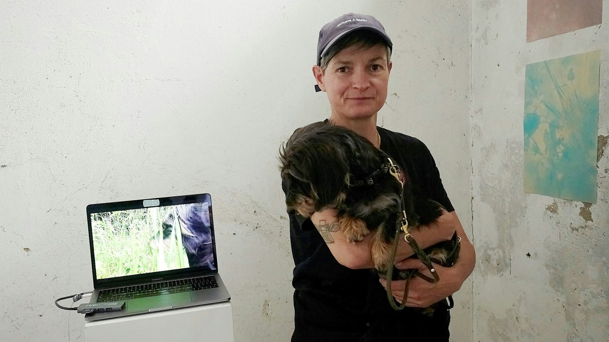 Jennifer De Negli hält einen Dackel auf dem Arm. Der hund schaut zu einem Laptop, der auf einem kleinen Tisch steht.