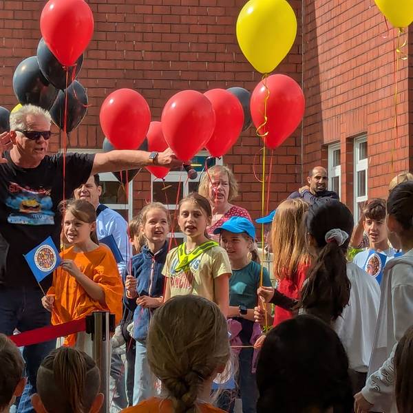 Das Foto zeigt einen Sänger in Pose vor Schulkindern, die Luftballons in der Hand halten.