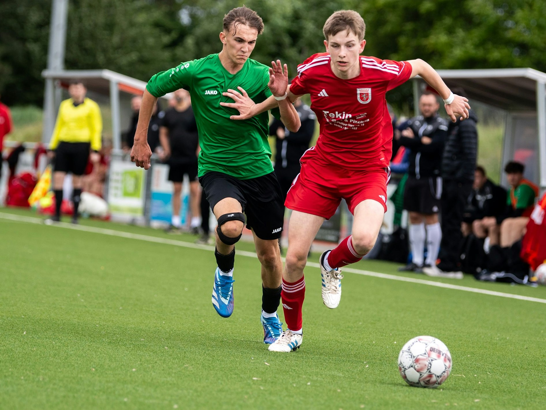 Zwei A-Junioren-Fußballer im Laufduell. Der eine versucht den anderen mit den Armen von sich fernzuhalten.