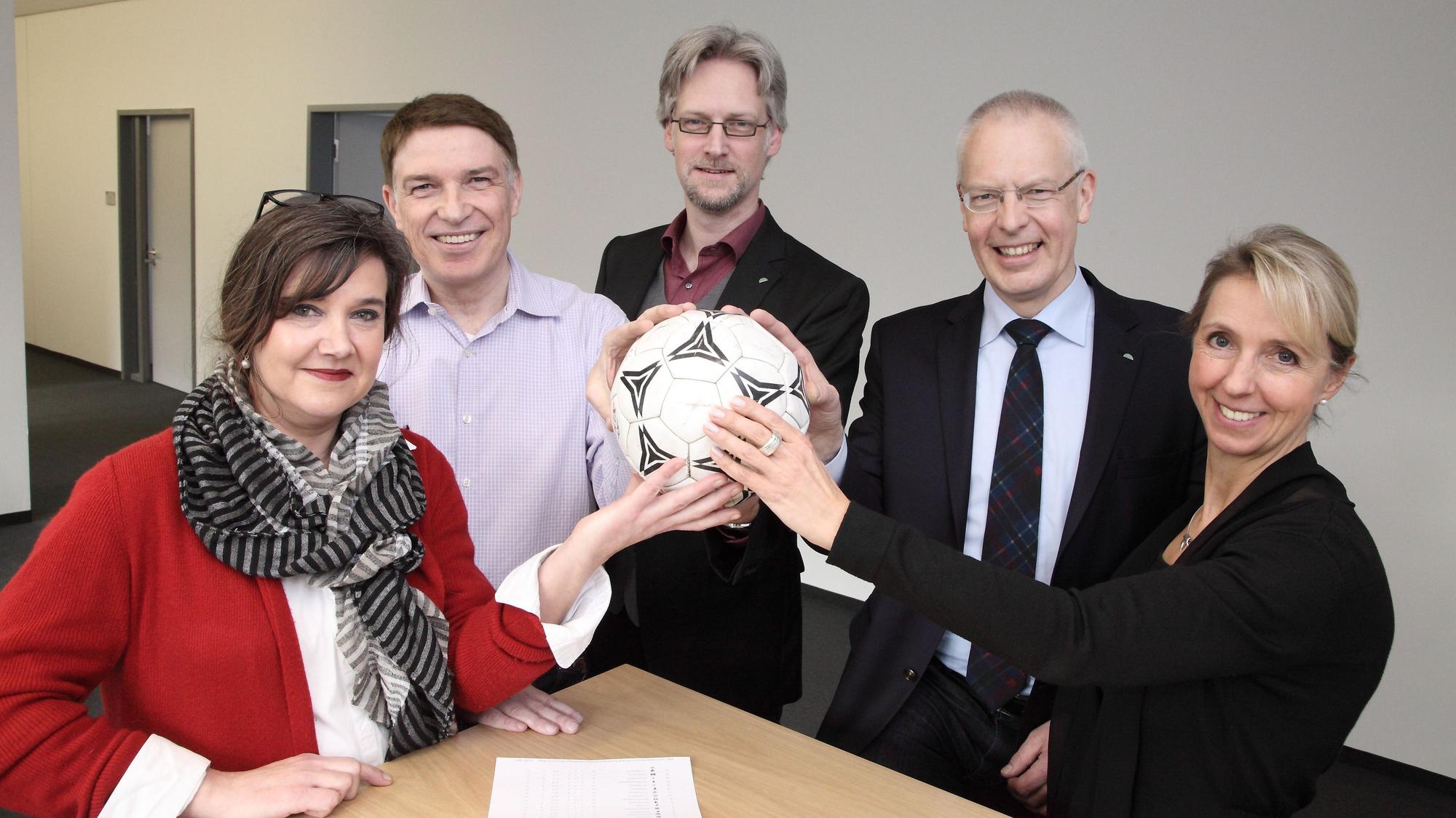 Fünf Menschen halten einen Fußball in den Händen.