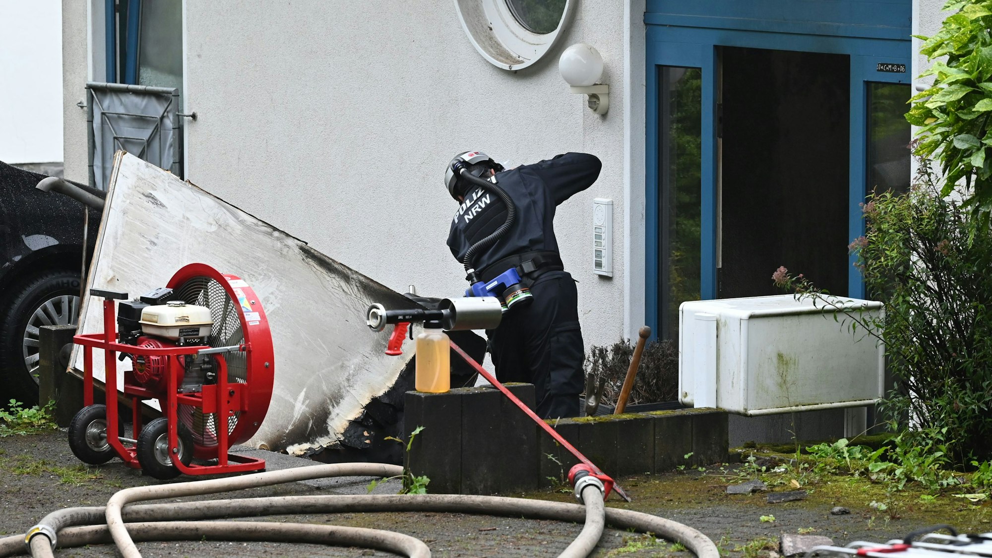 Ein Polizist in Schutzkleidung steht vor der Eingangstür eines Hauses in Bad Münstereifel-Holzem, in dem es gebrannt hat.