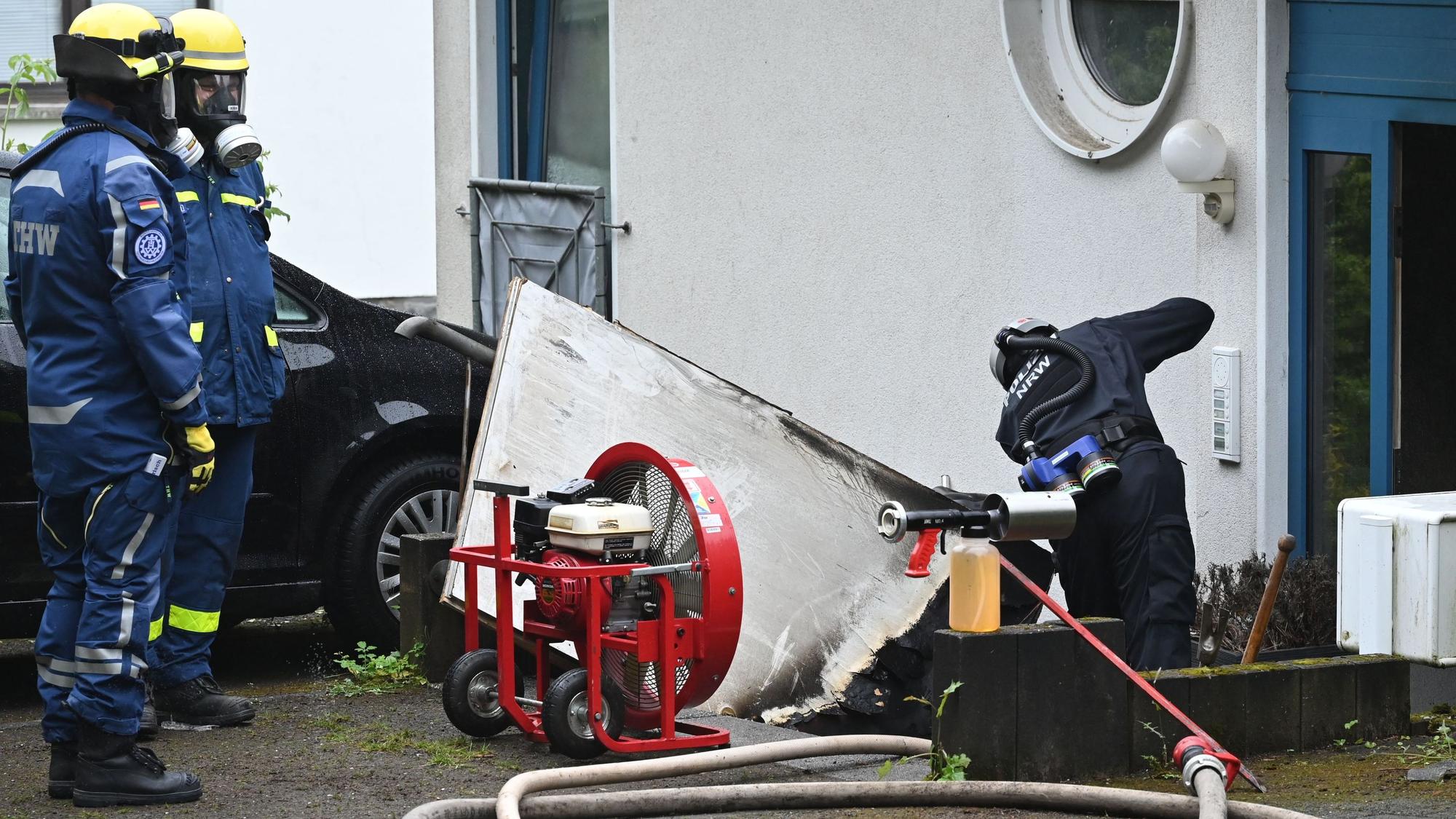 Ein Polizist steht vor der Eingangstür zu einem Mehrfamilienhaus. Zwei THW-Kräfte schauen ihm zu.