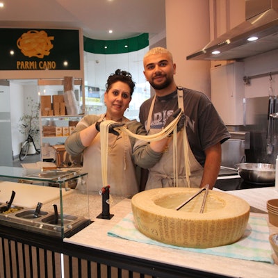Eine Frau und ein Mann an einer Bedienungstheke mit einem großen Käselaib.