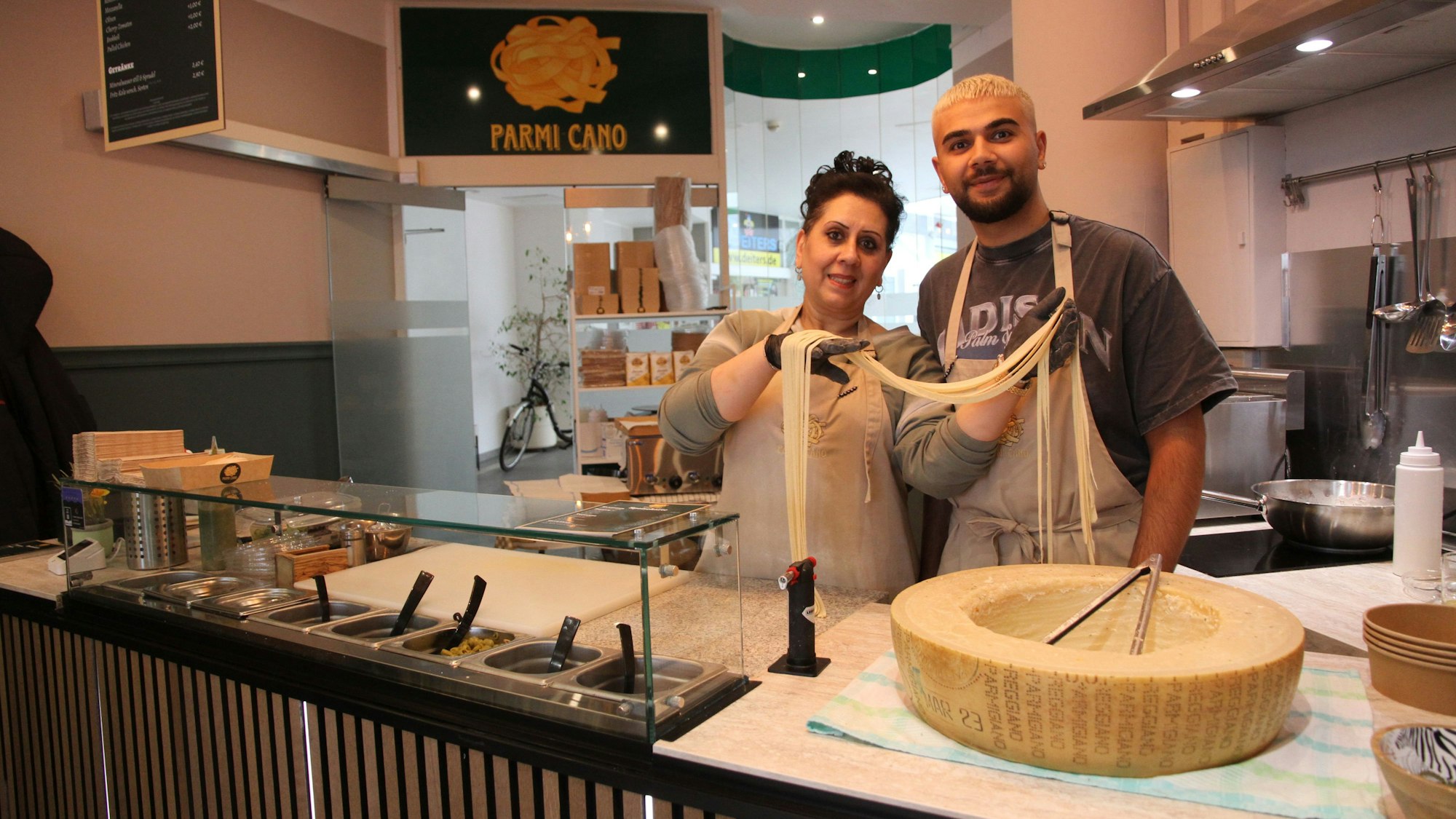 Eine Frau und ein Mann an einer Bedienungstheke mit einem großen Käselaib.