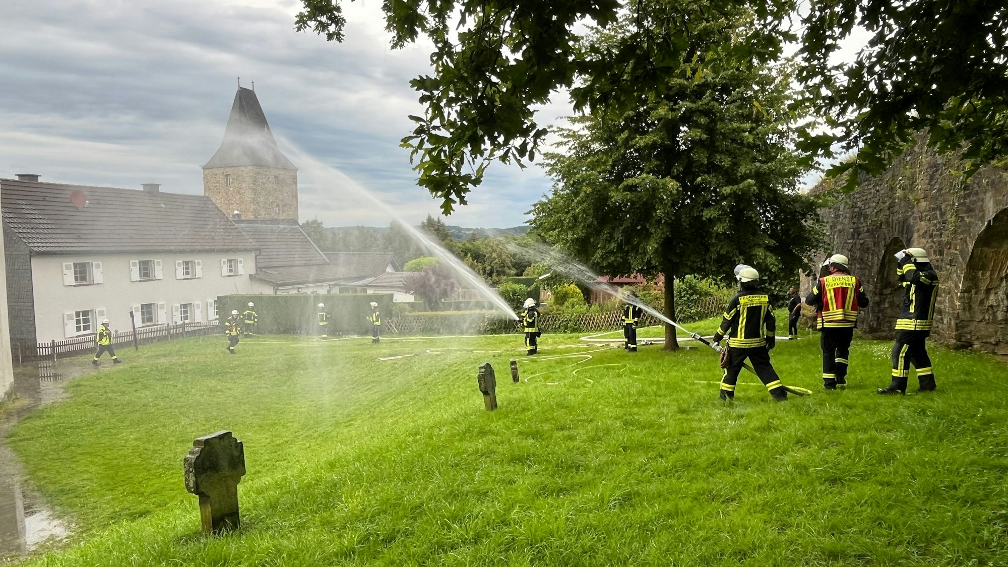 Feuerwehrleute halten mit ihren Schläuchen auf die Kirche und bauen eine Riegelstellung zum Schutz der angrenzenden Häuser auf.