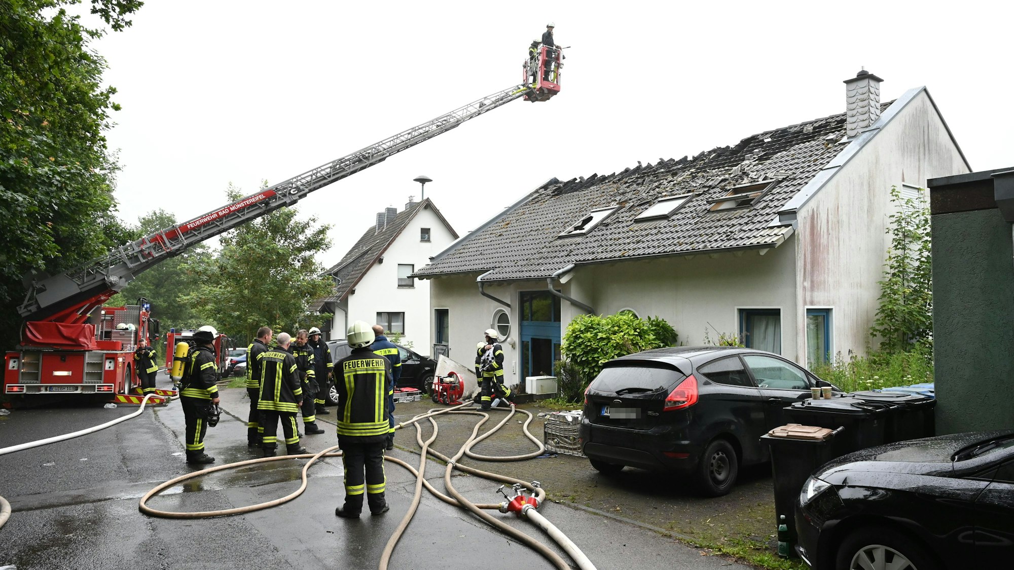 Zahlreiche Feuerwehrleute stehen in Bad Münstereifel-Holzem vor dem Haus, in dem es gebrannt hat. Das Dach ist schwer beschädigt.