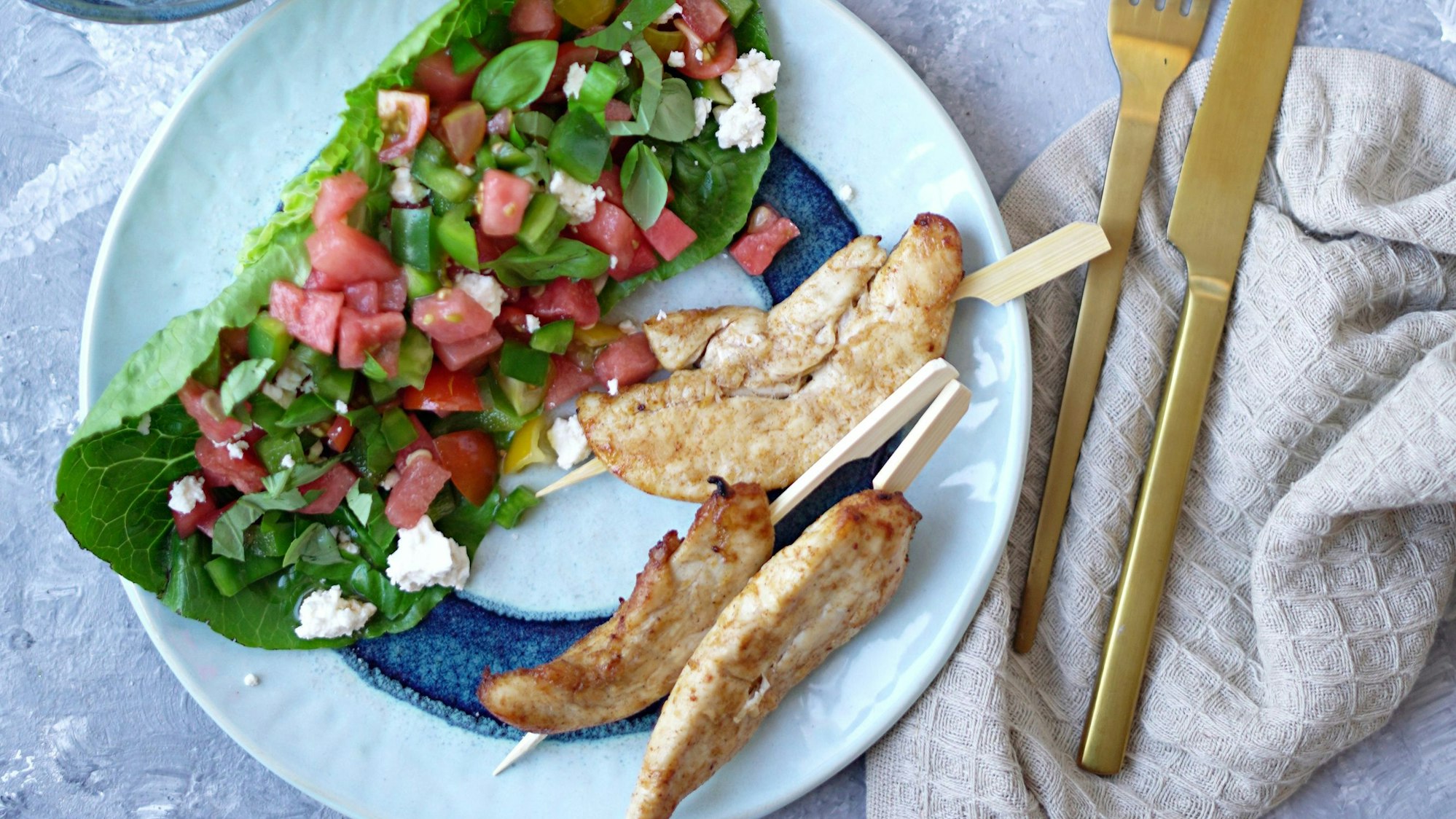 Auf einem Teller liegen Hähnchenspieße und die Wassermelonensalsa auf einem Salatblatt.