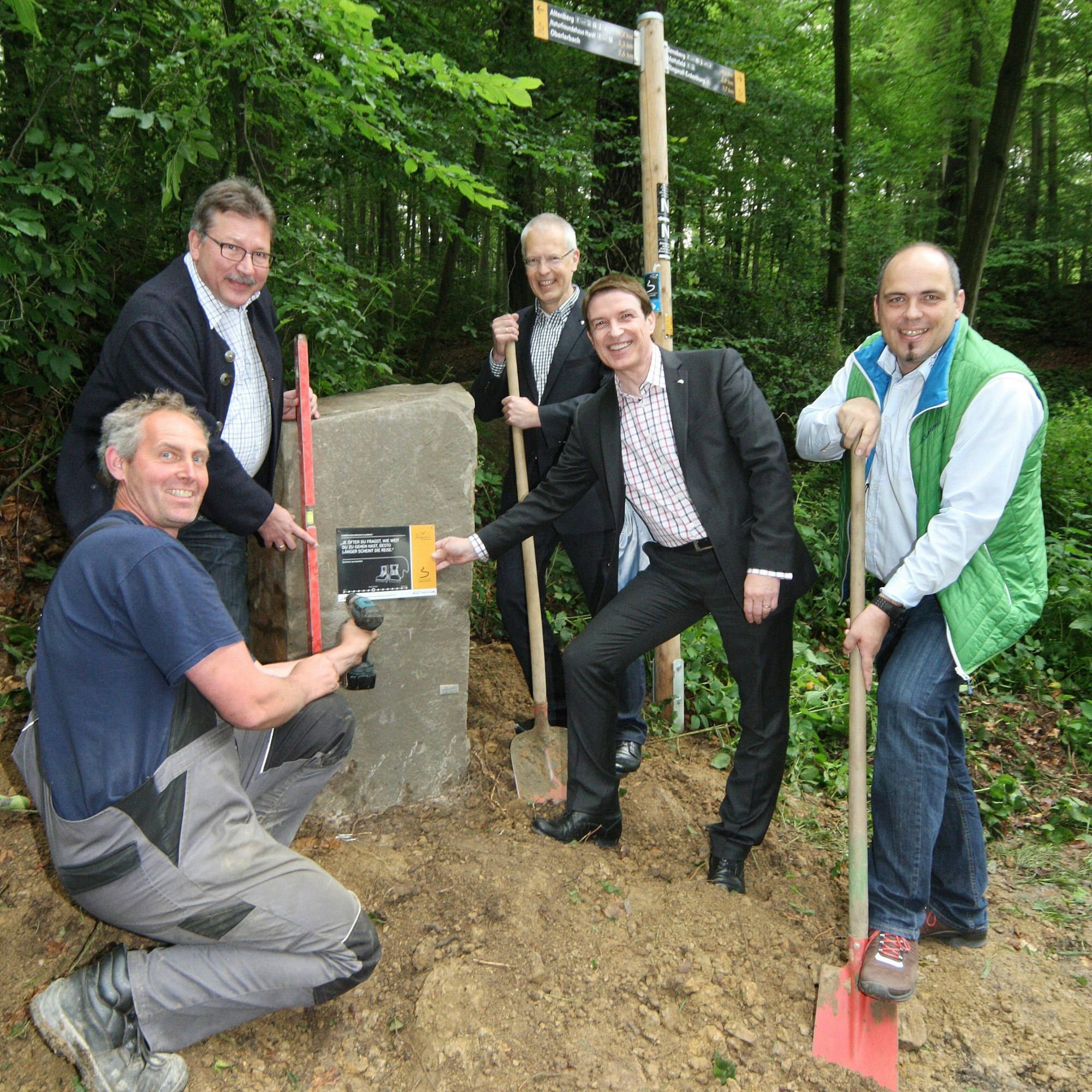 Mehrere Menschen stellen einen neuen Etappenstein an Etappenort des Bergischen Weg in Bergisch Gladbach-Bensberg auf.