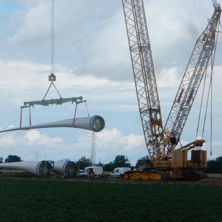 Ein Rotorblatt einer Windkraftanlage wird von einem Kran angehoben.