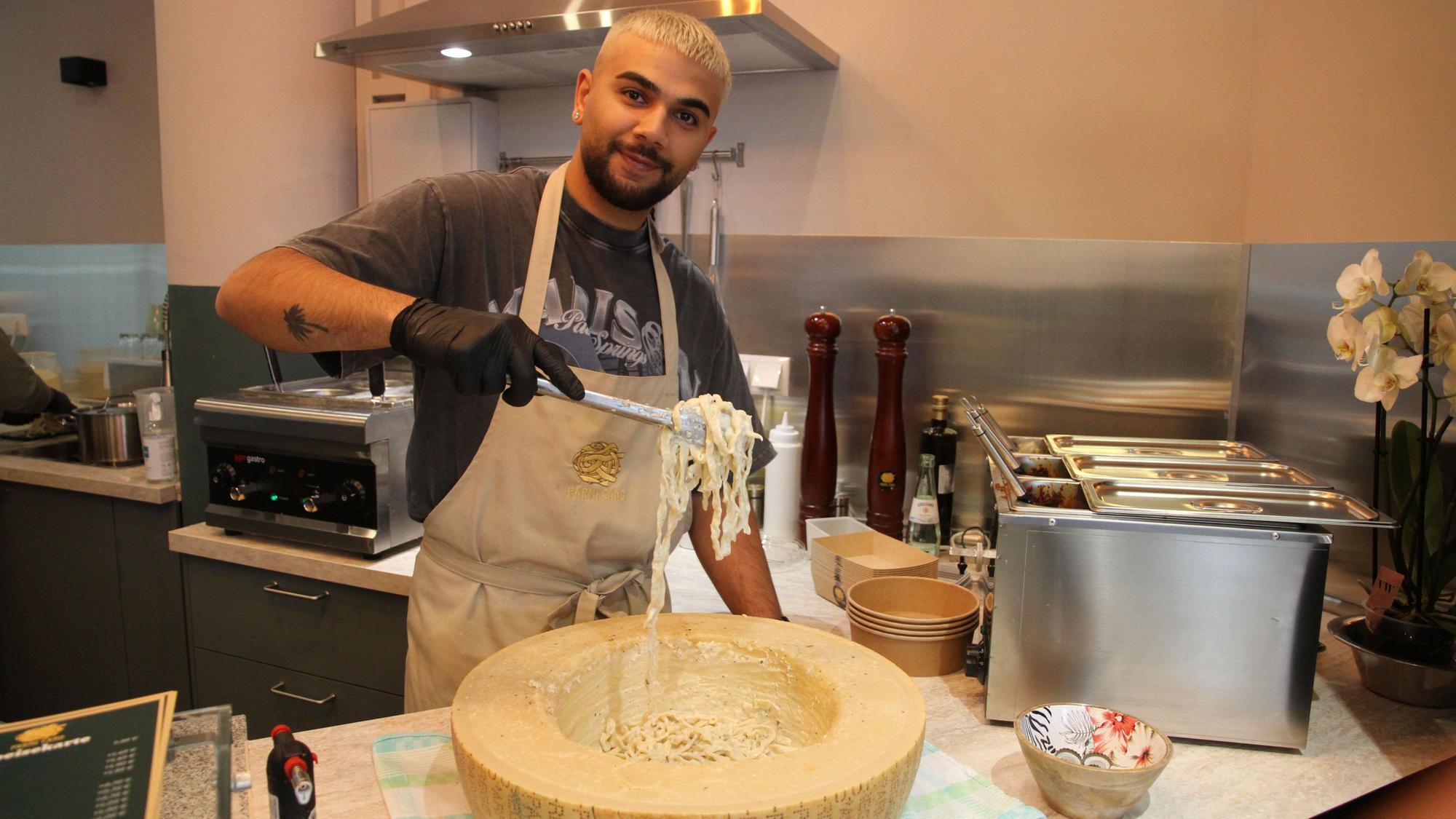 Ein Mann schwenkt Nudeln durch eine Kuhle in einem Parmesan-Rad.