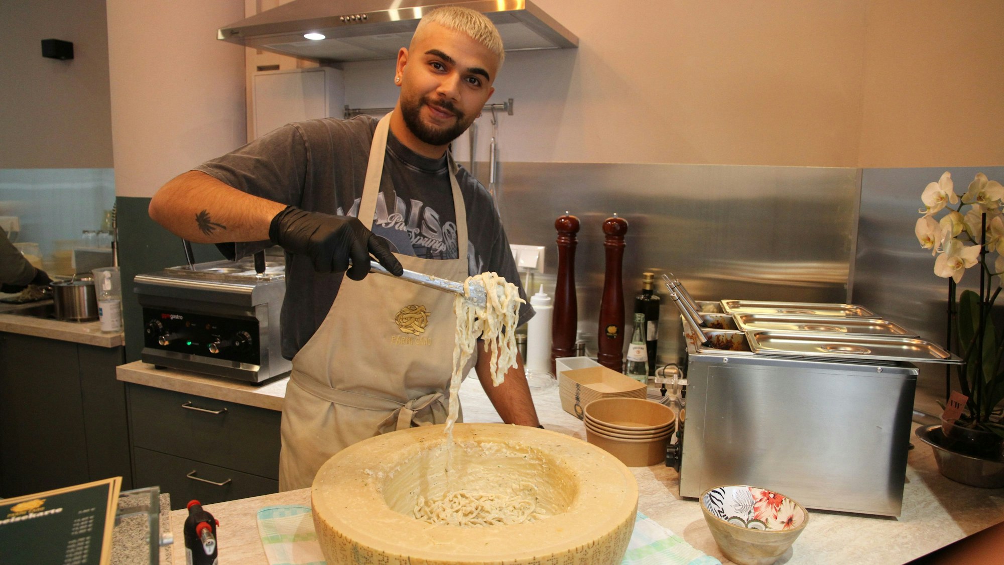 Ein Mann schwenkt Nudeln durch eine Kuhle in einem Parmesan-Rad.