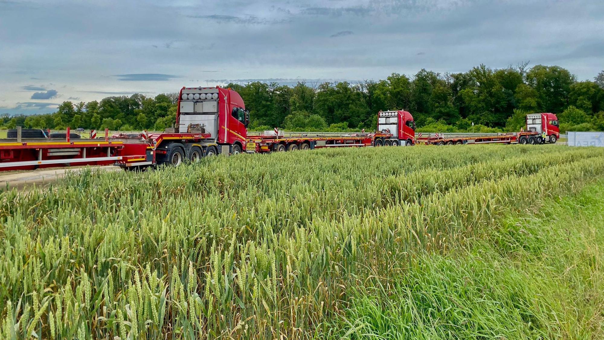 Drei rote Schwertransporter stehen hintereinander geparkt auf einem Feldweg.