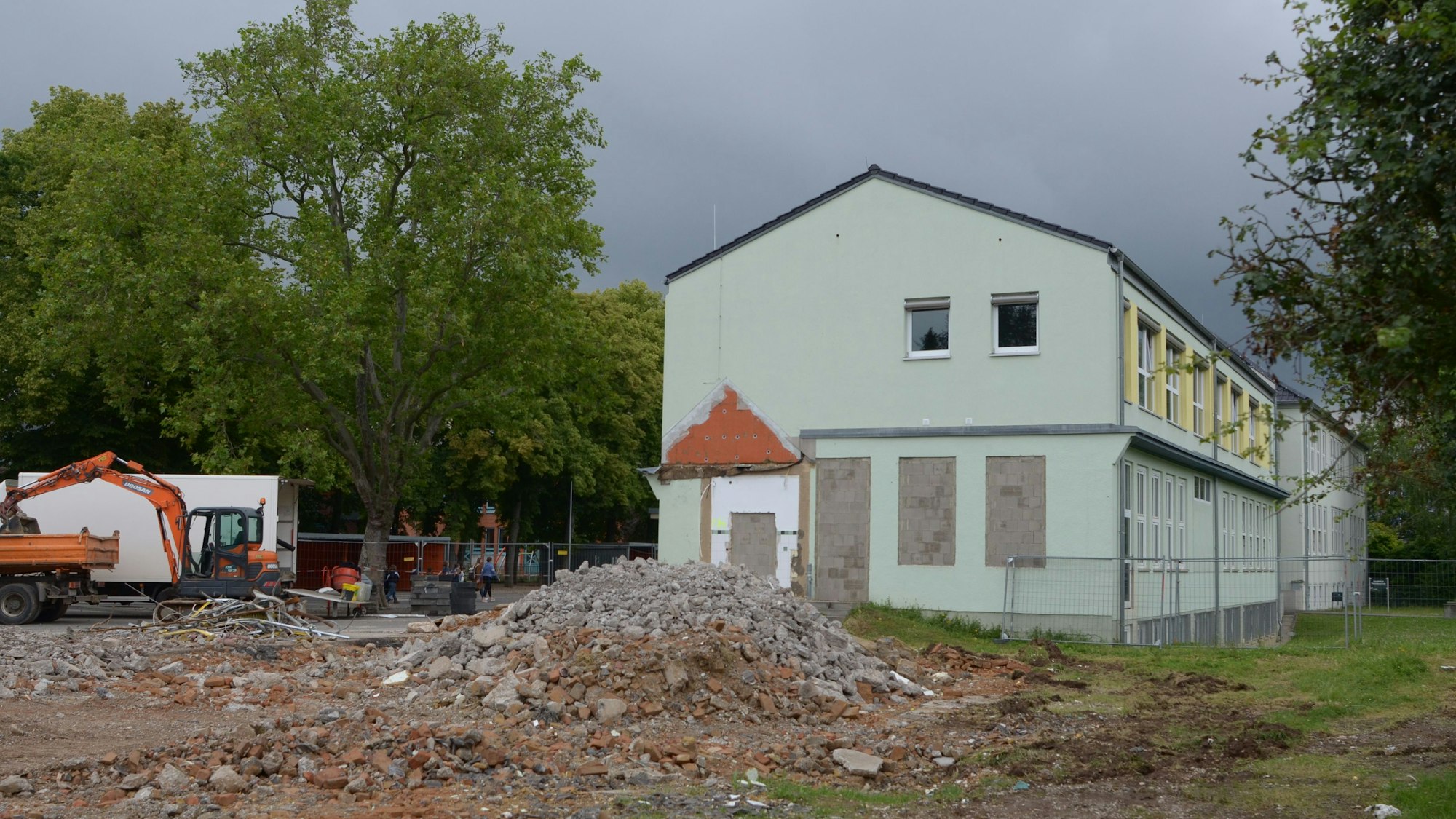 Auf dem Schulgelände liegt Bauschutt, am Bildrand ist ein Bagger zu sehen.