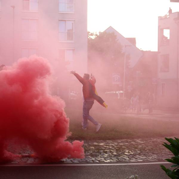 Eine rote Wolke ist auf dem Europaplatz zu sehen. Ein Fan läuft jubelnd über den Platz, er ist von dem Rauch eingehüllt.