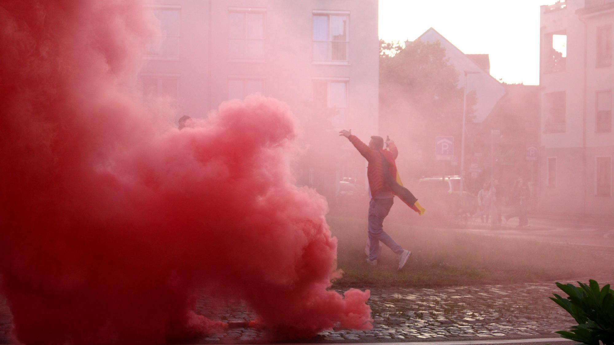 Eine rote Wolke ist auf dem Europaplatz zu sehen. Ein Fan läuft jubelnd über den Platz, er ist von dem Rauch eingehüllt.