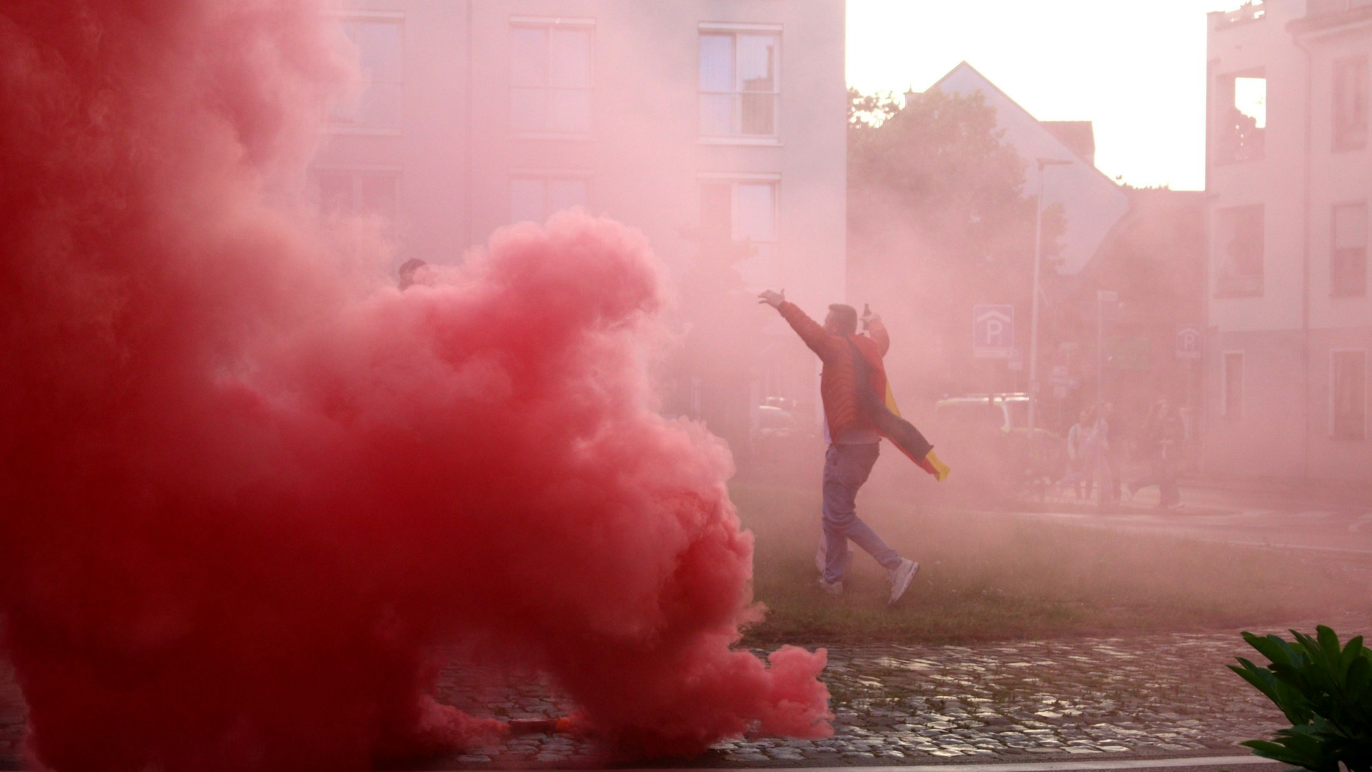 Eine rote Wolke ist auf dem Europaplatz zu sehen. Ein Fan läuft jubelnd über den Platz, er ist von dem Rauch eingehüllt.