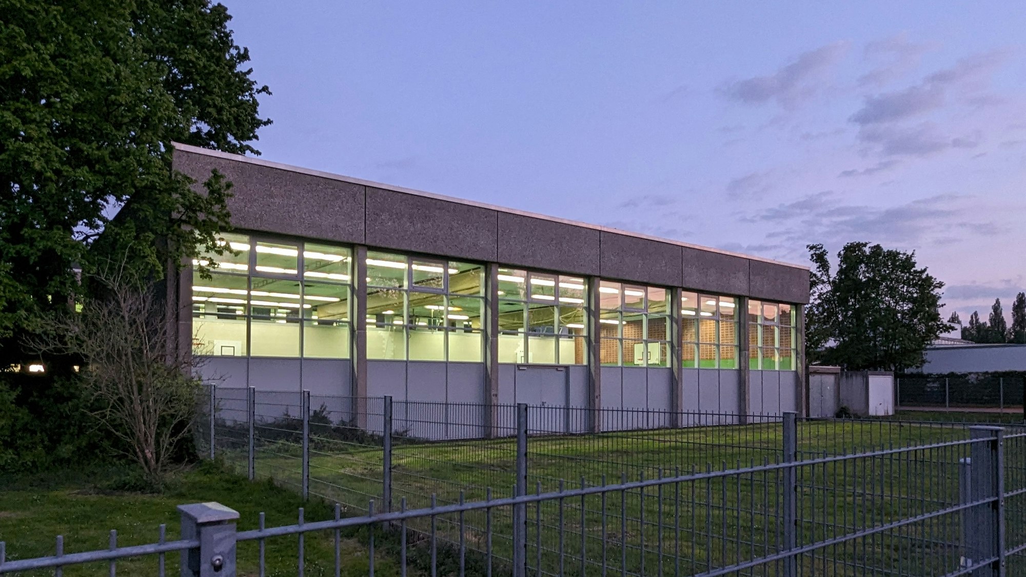 Die Außenansicht einer beleuchteten Turnhalle bei Dämmerung.