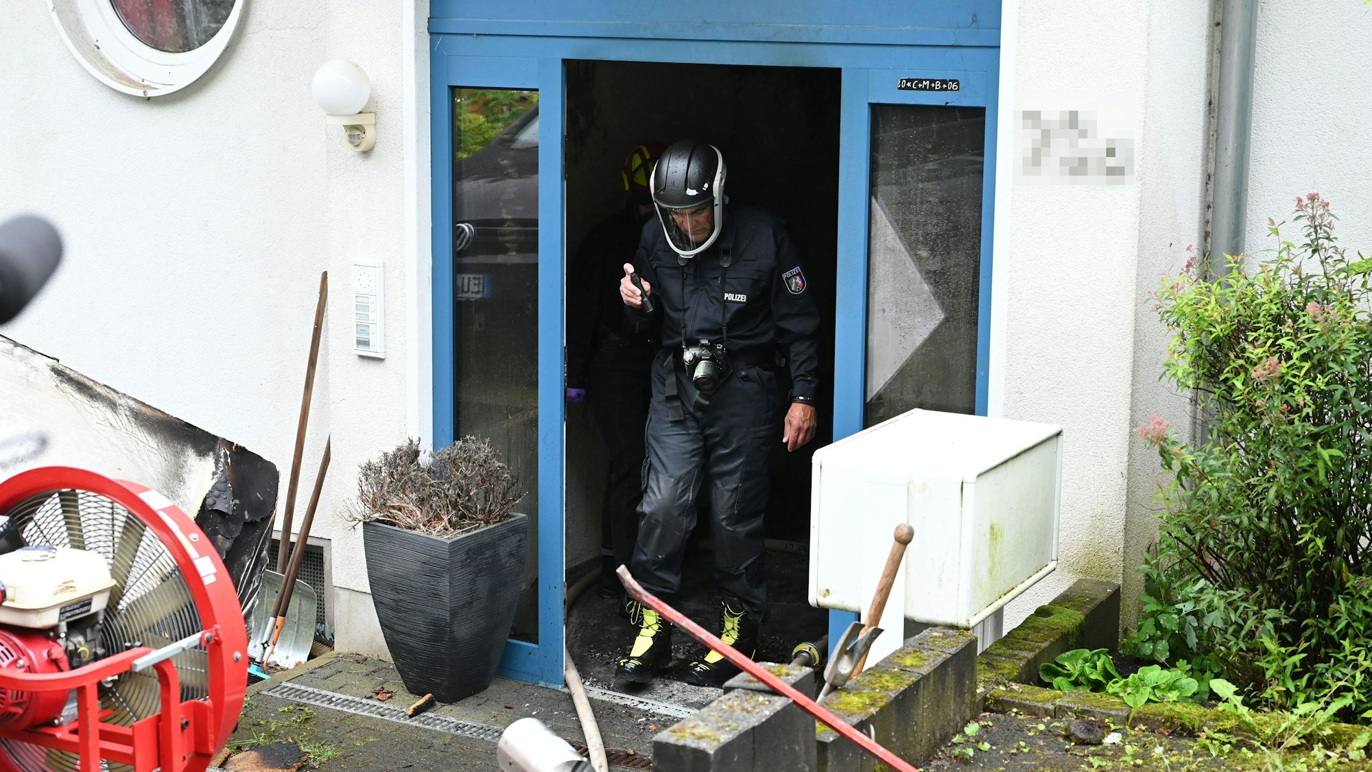 Ein Brandermittler der Polizei, der einen Helm und Atemschutz trägt, geht durch die Eingangstür des noch verrauchten Hauses.