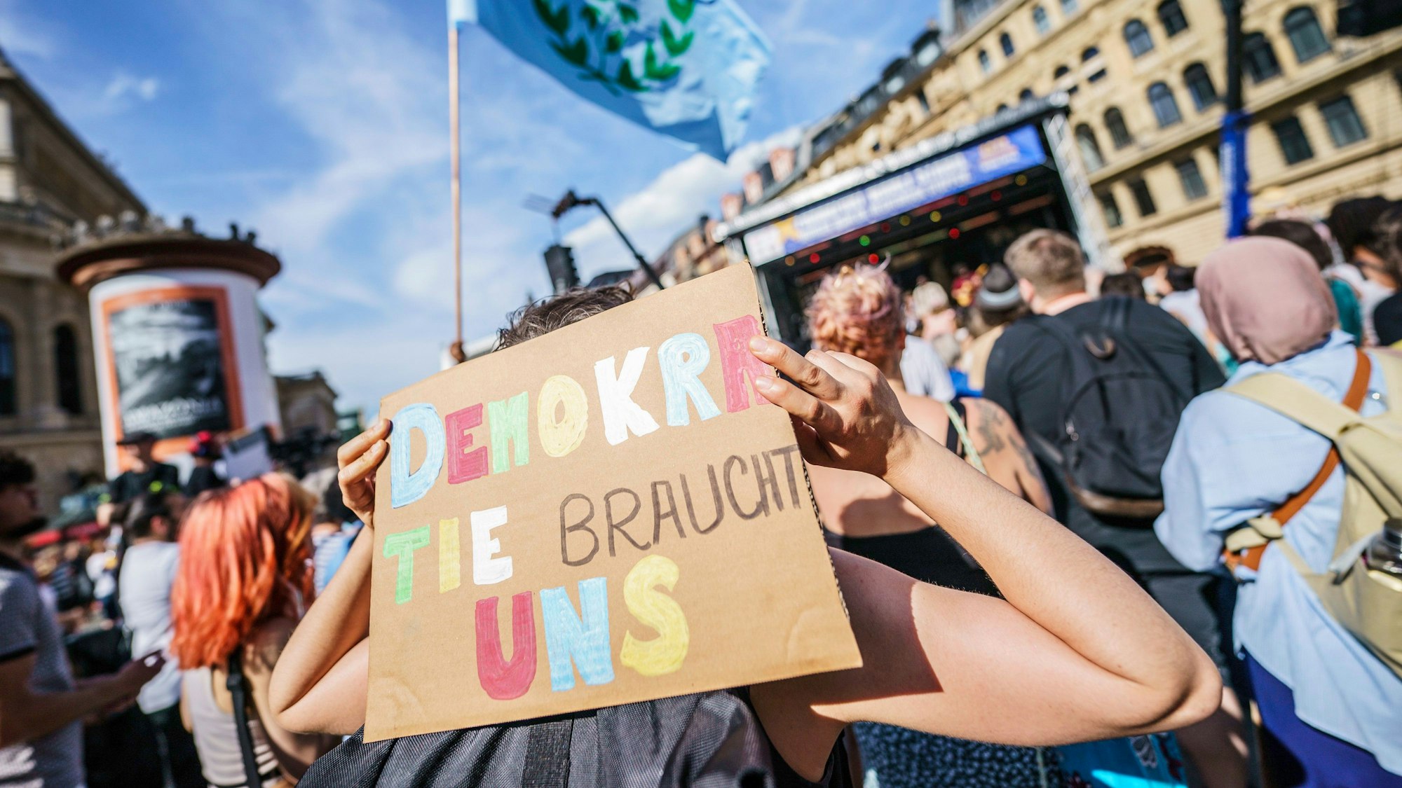 Ein Plakat mit der Aufschrift „Demokratie braucht uns“ wird hochgehalten.