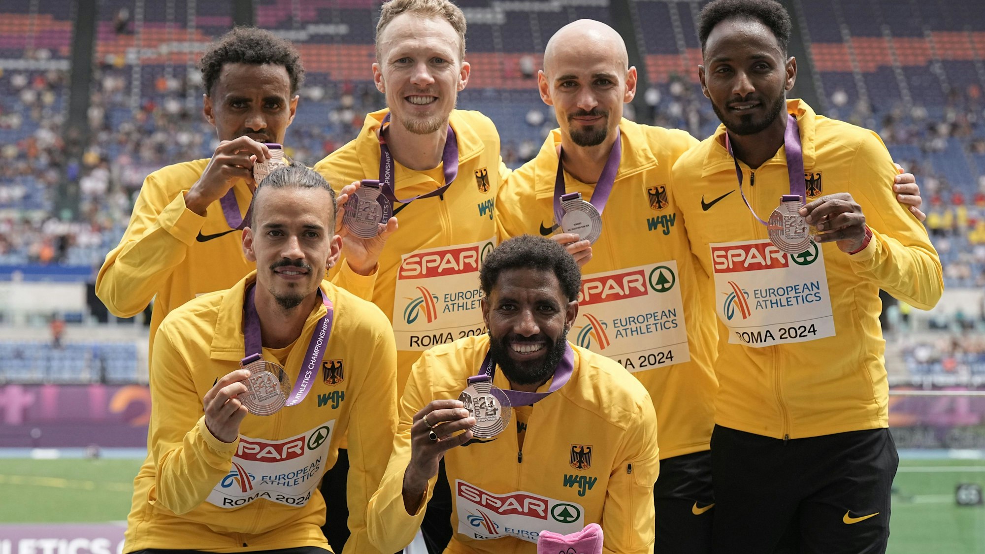 Sechs Sportler in gelben Trainingsjacken halten ihre Bronzemedaillen in die Kamera, die sie bei der Europameisterschaft in Rom gewonnen haben.