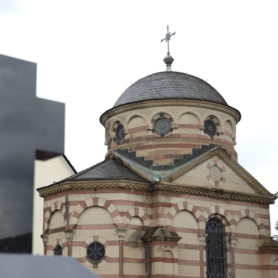 Im Vordergrund ein Kreuz, im Hintergrund ein Gebäude mit einer Kuppel.