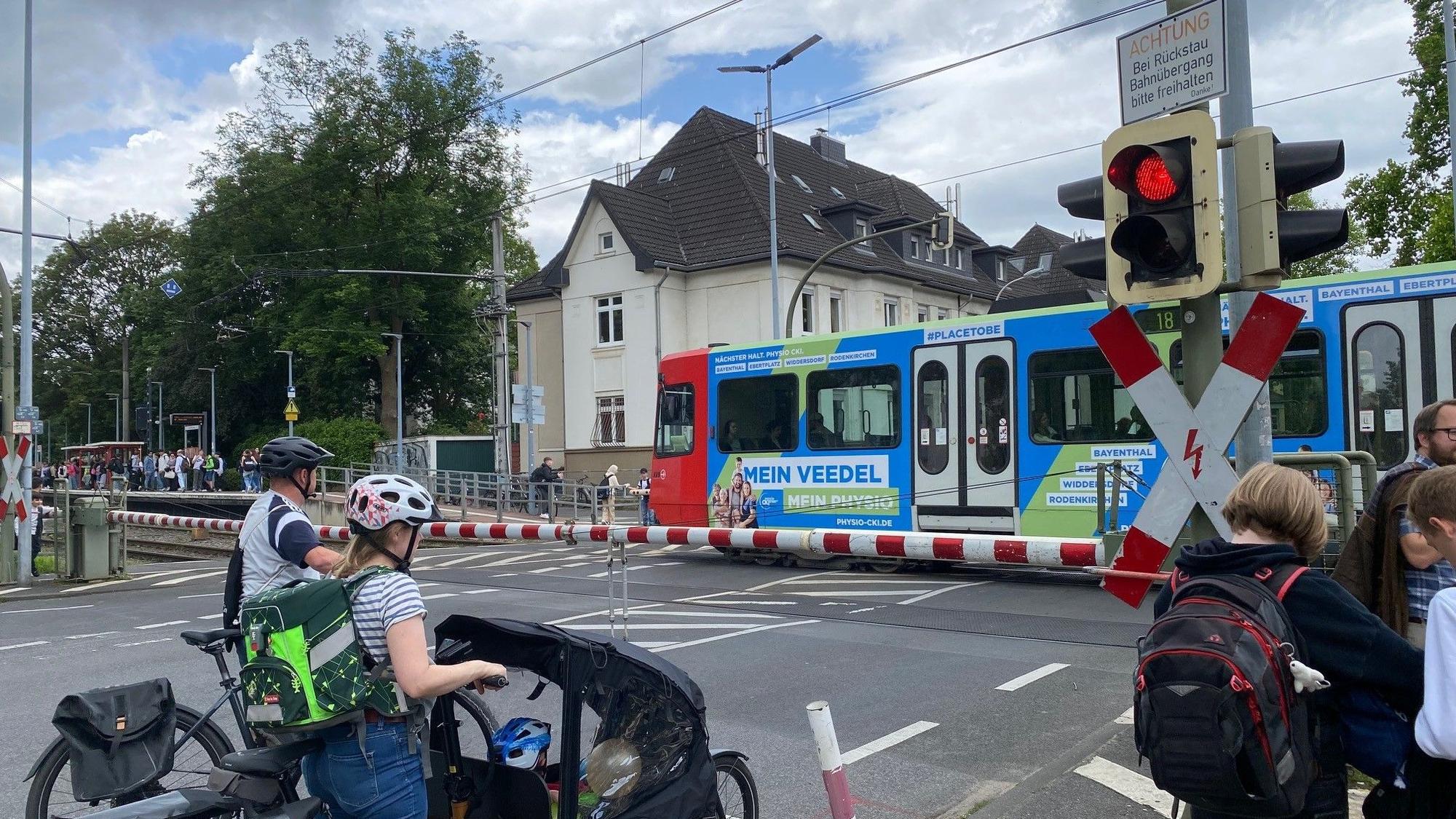 Zu sehen sind Menschen, die am geschlossenen Bahnübergang warten.