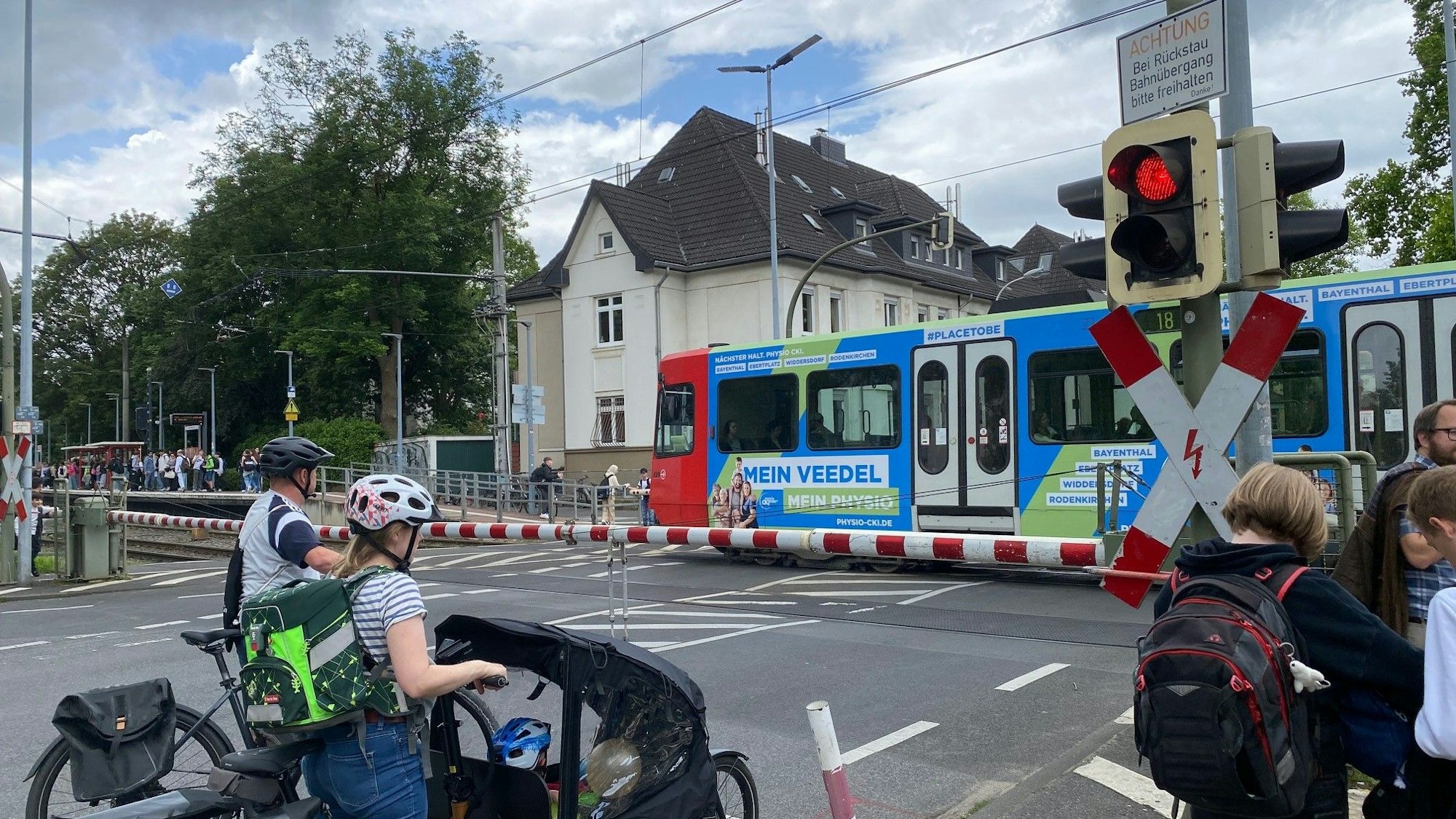 Zu sehen sind Menschen, die am geschlossenen Bahnübergang warten.