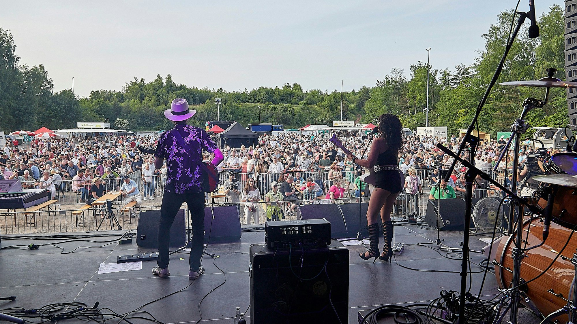 Eine Band spielt auf einer Bühne, vor der zahlreiche Zuschauer stehen.