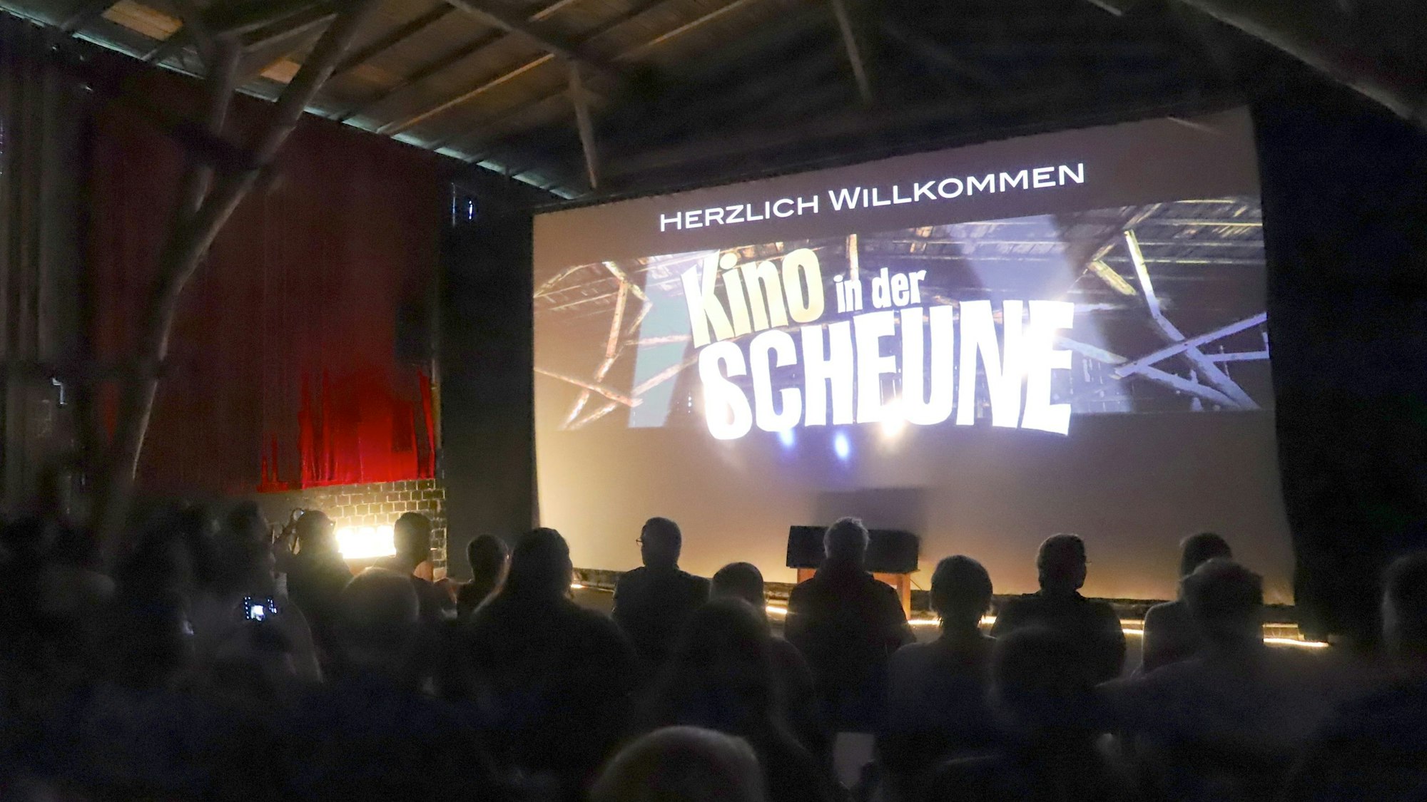 Menschen sitzen in einer Scheune vor einer großen Leinwand.