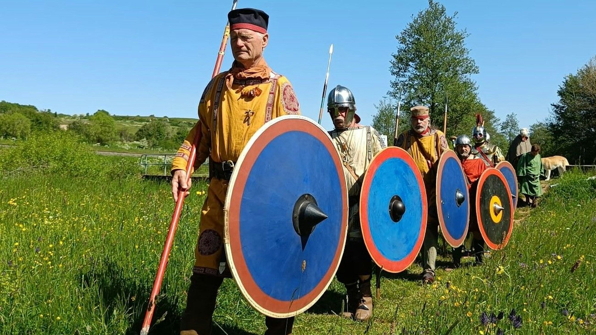 Männer in historischen Kostümen mit Schild und Speer laufen über eine Wiese