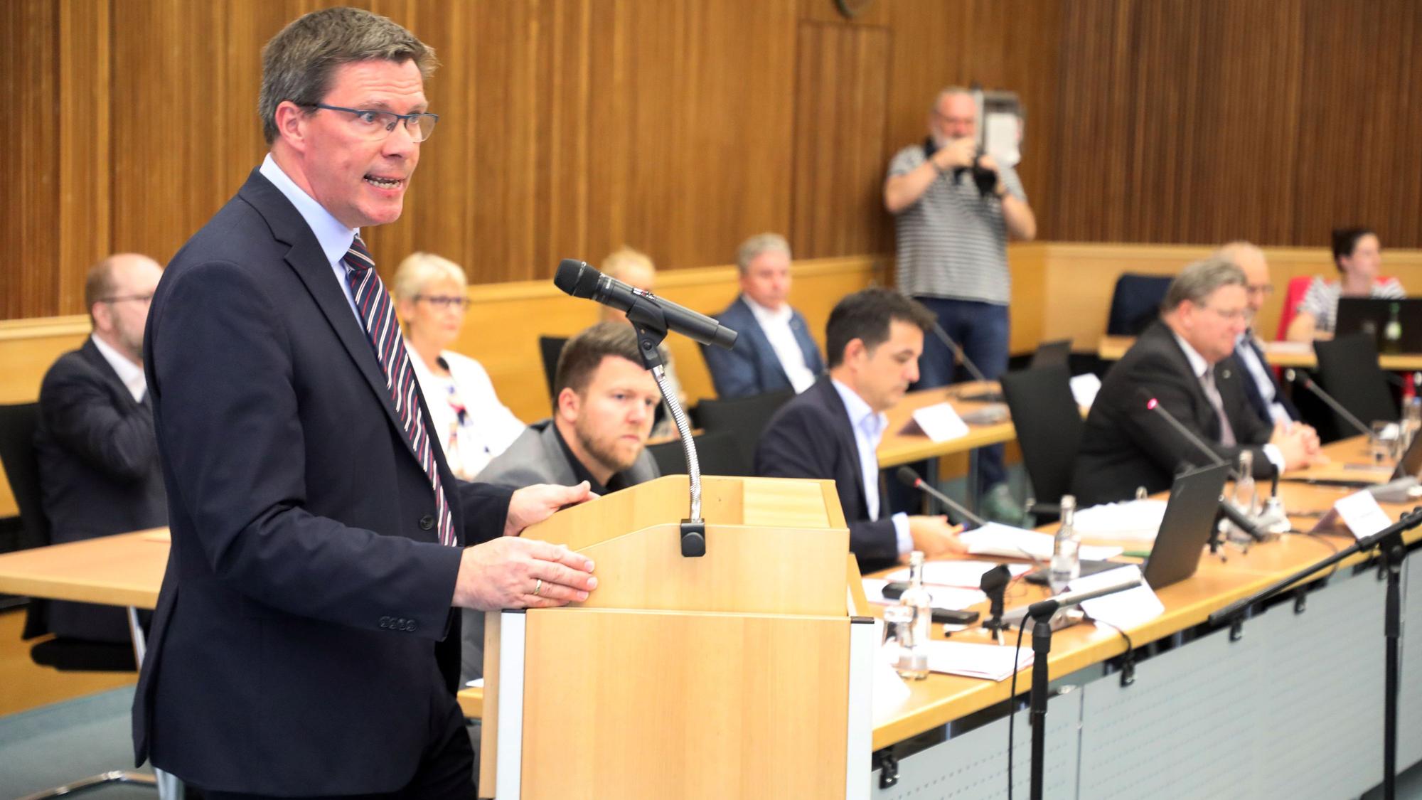 Landrat Stephan Santelmann steht am Rednerpult im großen Sitzungssaal des Kreishauses am Rübezahlwald.