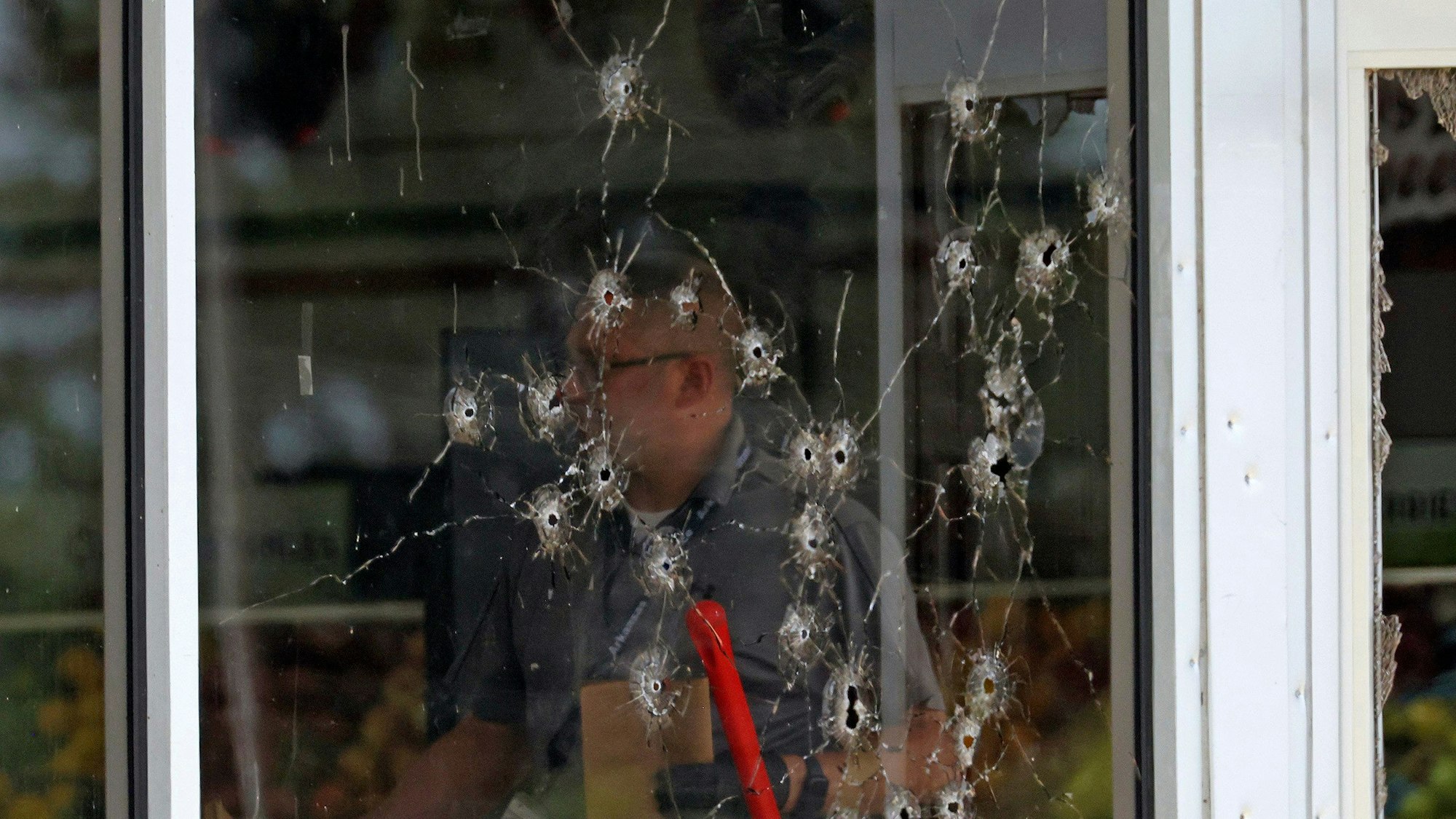 Einschusslöcher sind an einer Fensterfront zu sehen, als Polizeibeamte den Tatort nach Schüssen am «Mad Butcher»-Lebensmittelgeschäft untersuchen.
