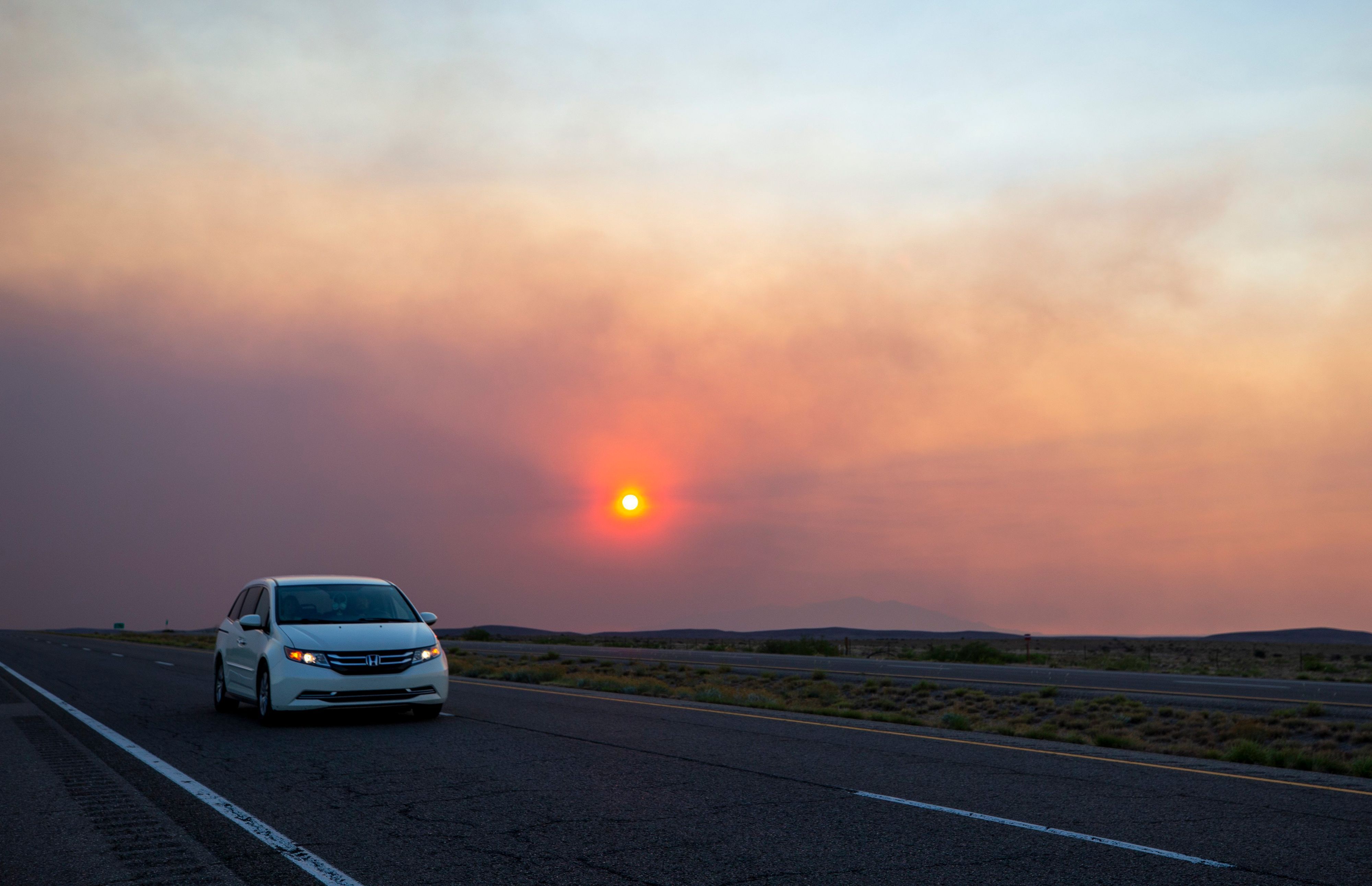 Ein Auto auf einer Straße, im Hintergrund Rauch eines Waldbrandes. (Symbolbild)
