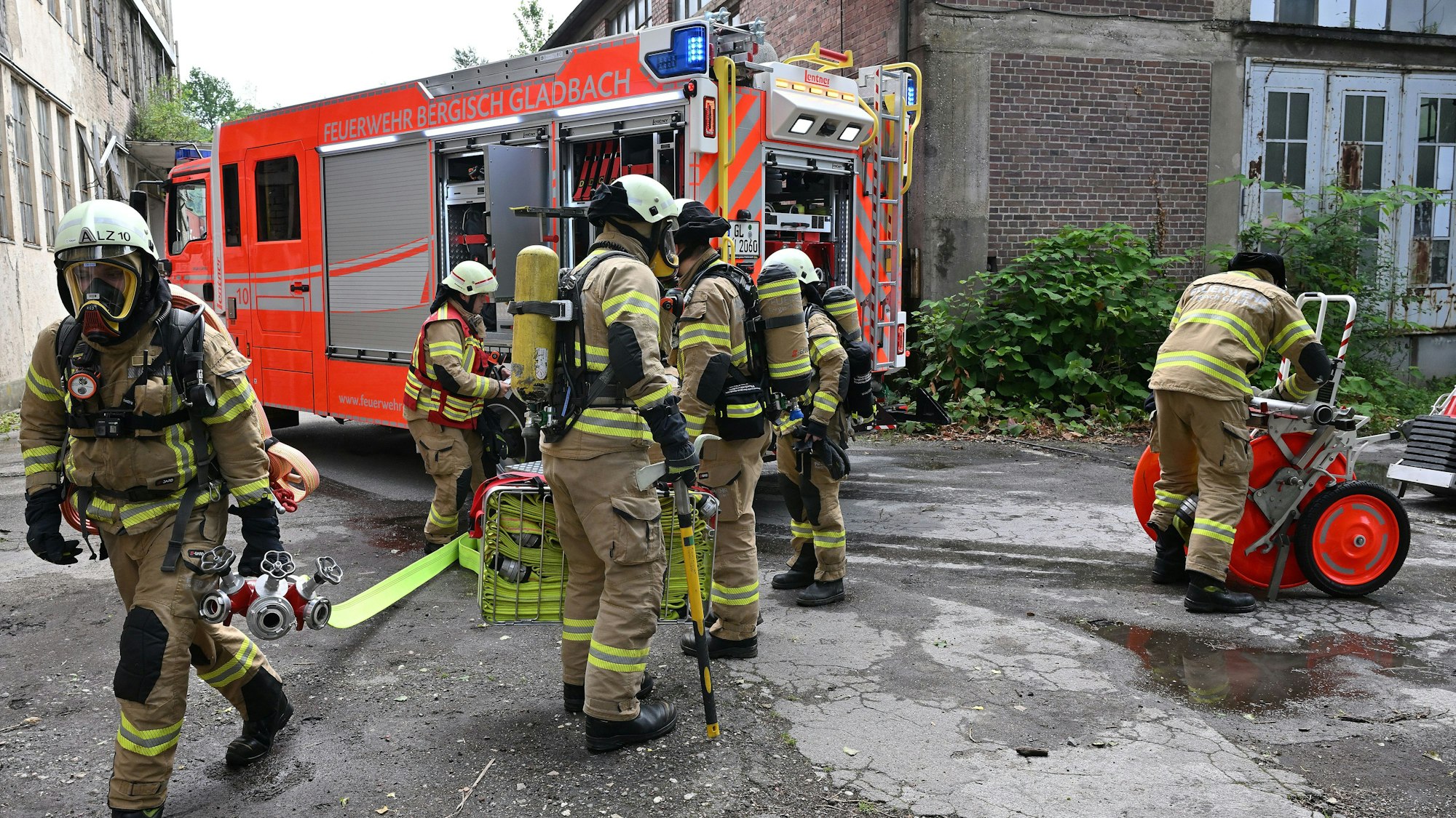 Feuerwehrleute unter Atemschutz gehen von einem Feuerwehrfahrzeug auf ein Haus zu.