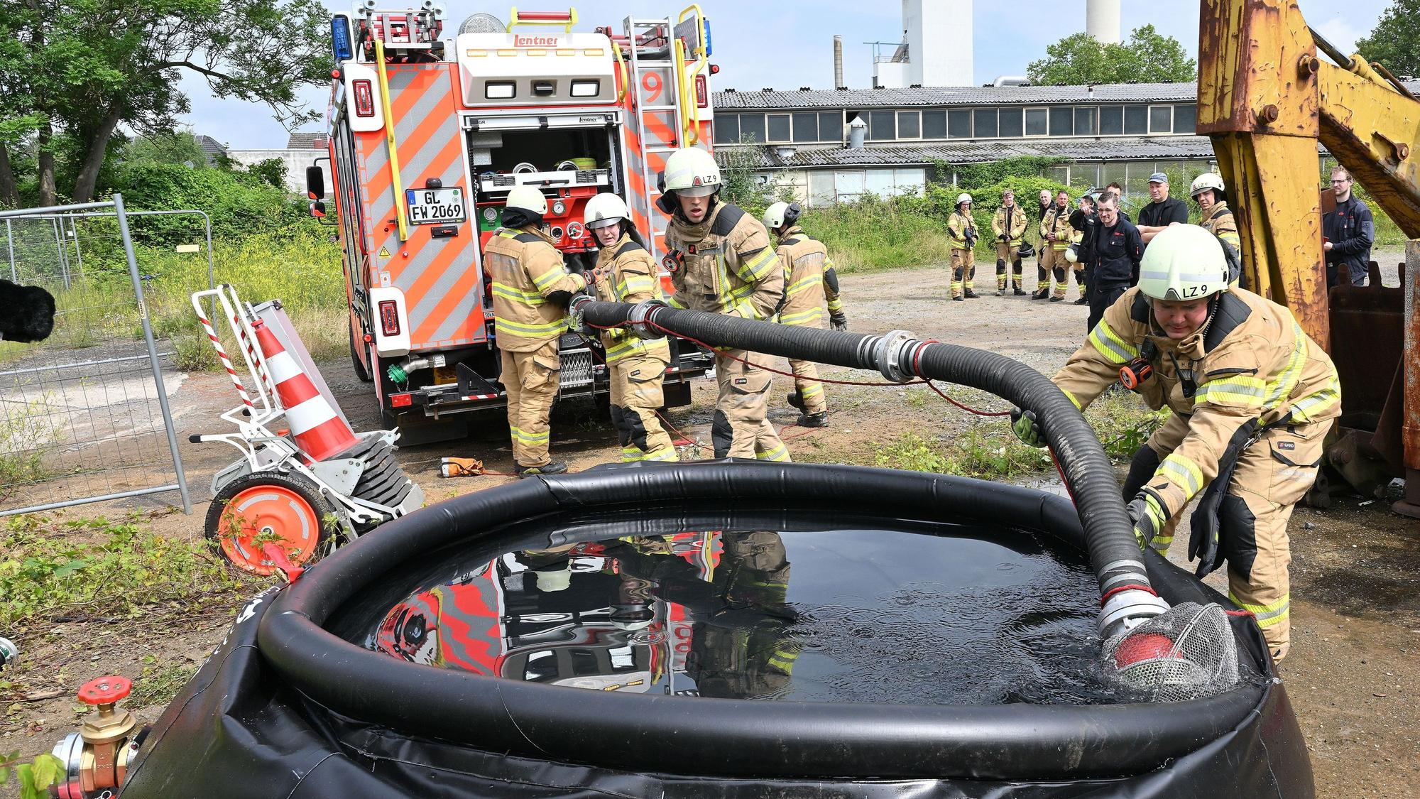 Feuerwehrleute legen eine Saugleitung von einem Feuerwehrfahrzeug in ein großes Wasserbassin.