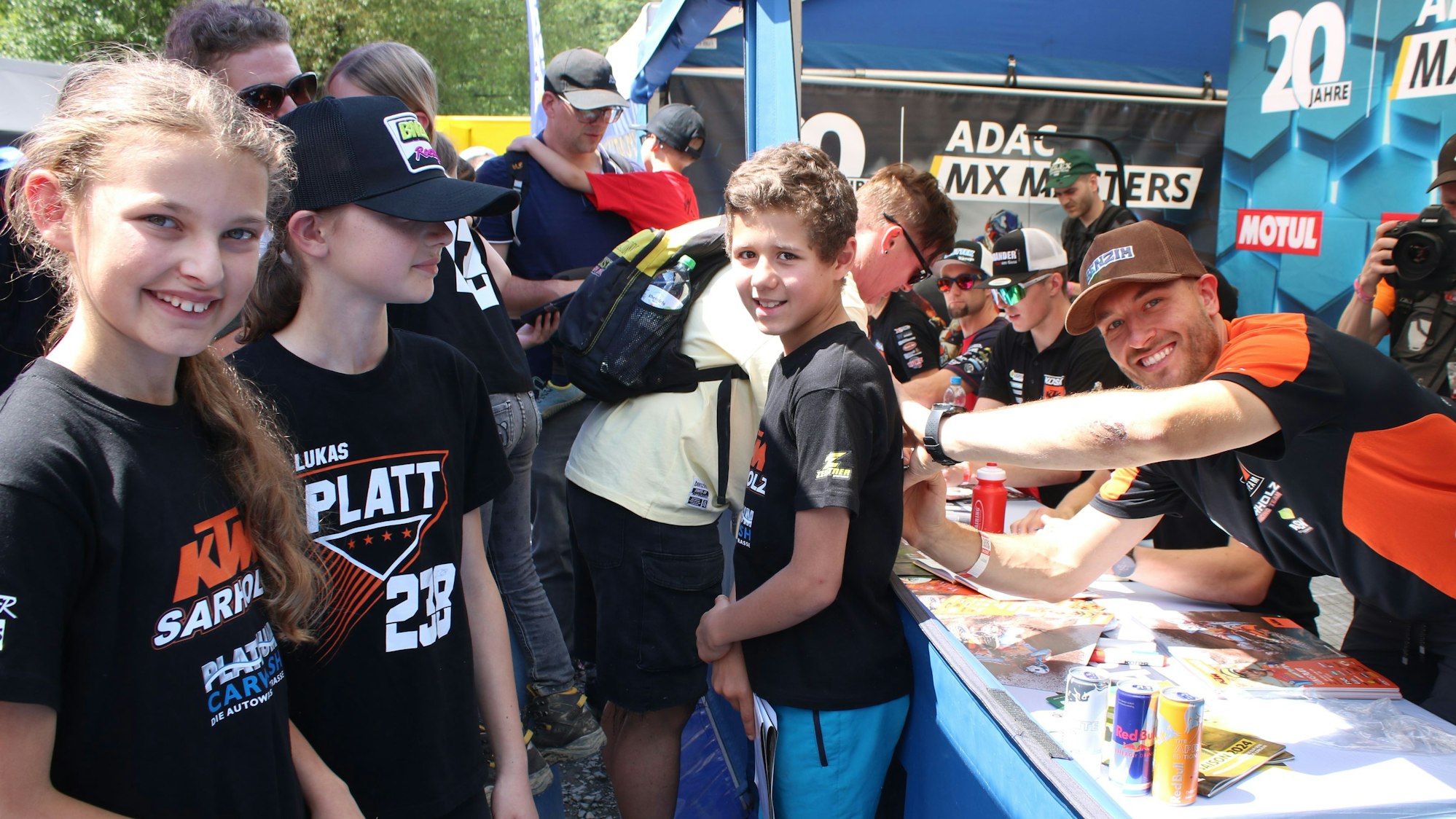 Motocrosser Lukas Platt lacht in die Kamera während er ein T-Shirt signiert.