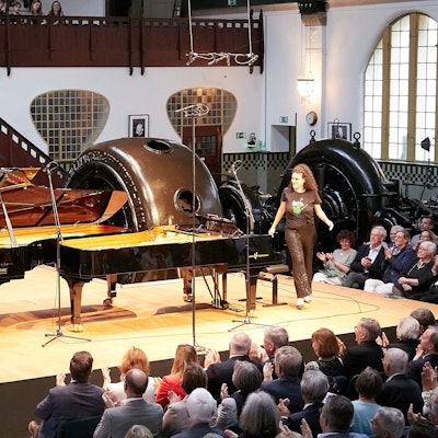 Die Schwestern Danae und Kiveli Dörken stehen neben zwei Flügeln auf einer Bühne, im Hintergrund sind Turbinen erkennbar.